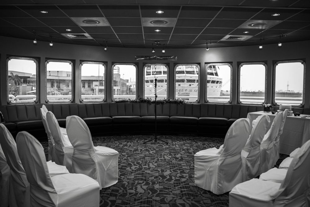 Interior view of an elegant boat cabin with white-covered chairs and large windows showing harbor views. Micro wedding on Yacht StarShip in