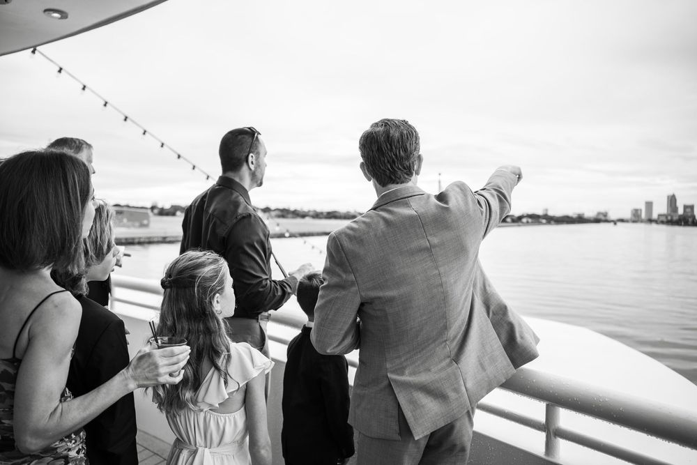 A group of people stand together at a railing looking out over a scenic view in black and white. Micro wedding on Yacht StarShip in Tampa