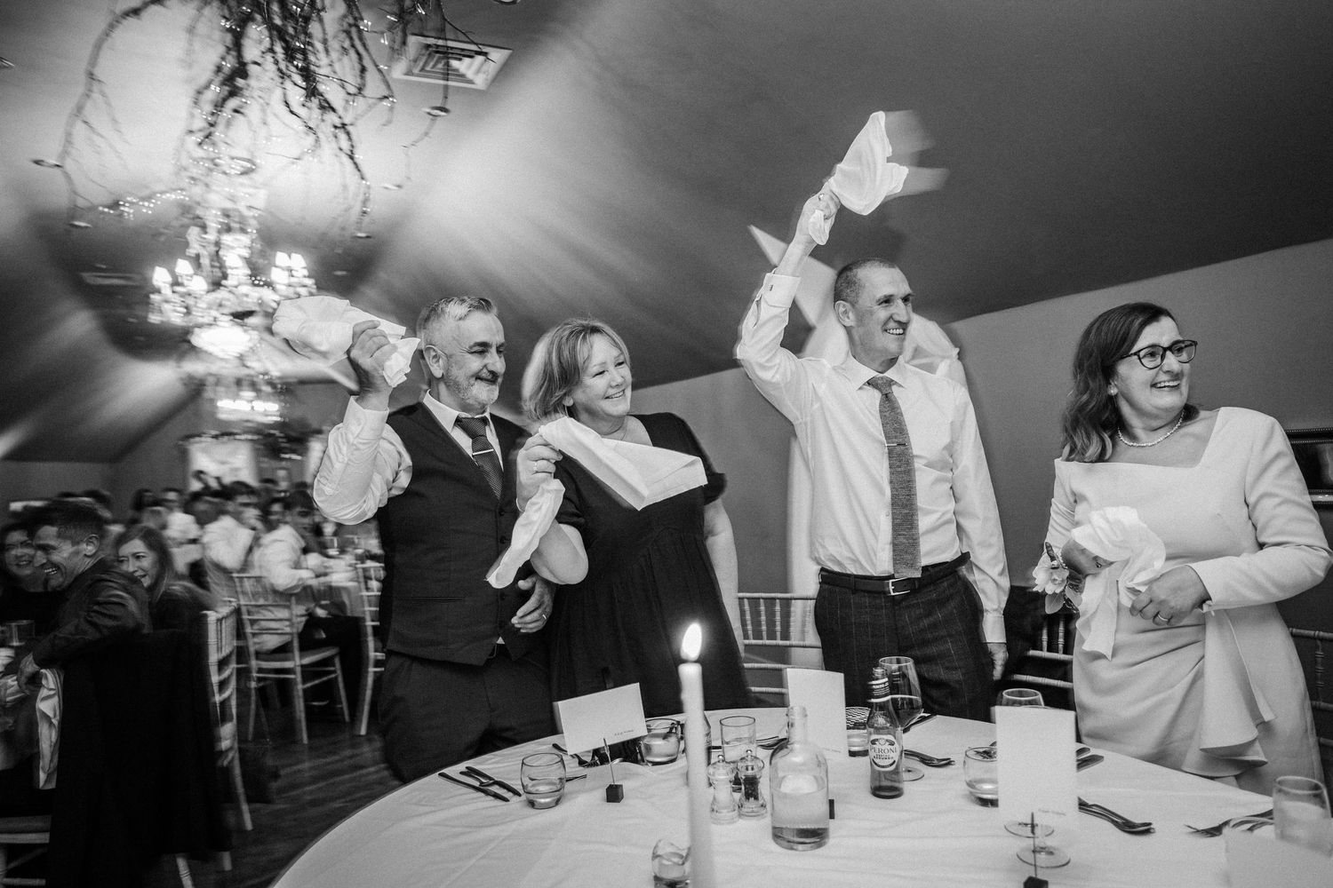 Wedding guests enjoying a lively reception celebration at tables in a dimly lit venue.
