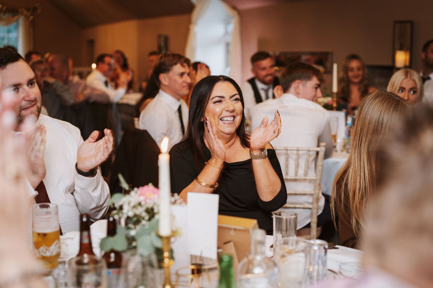 Wedding guests enjoying a lively reception dinner at elegantly decorated tables with glowing candlelight.