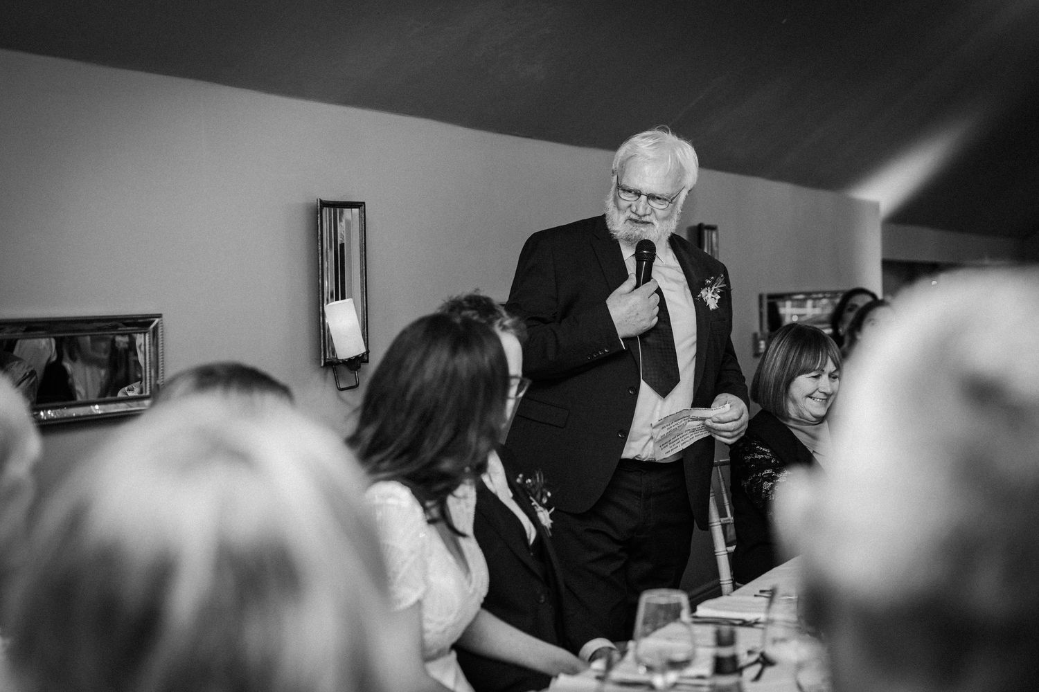 Black and white photo of wedding guests mingling and socializing during an indoor celebration.