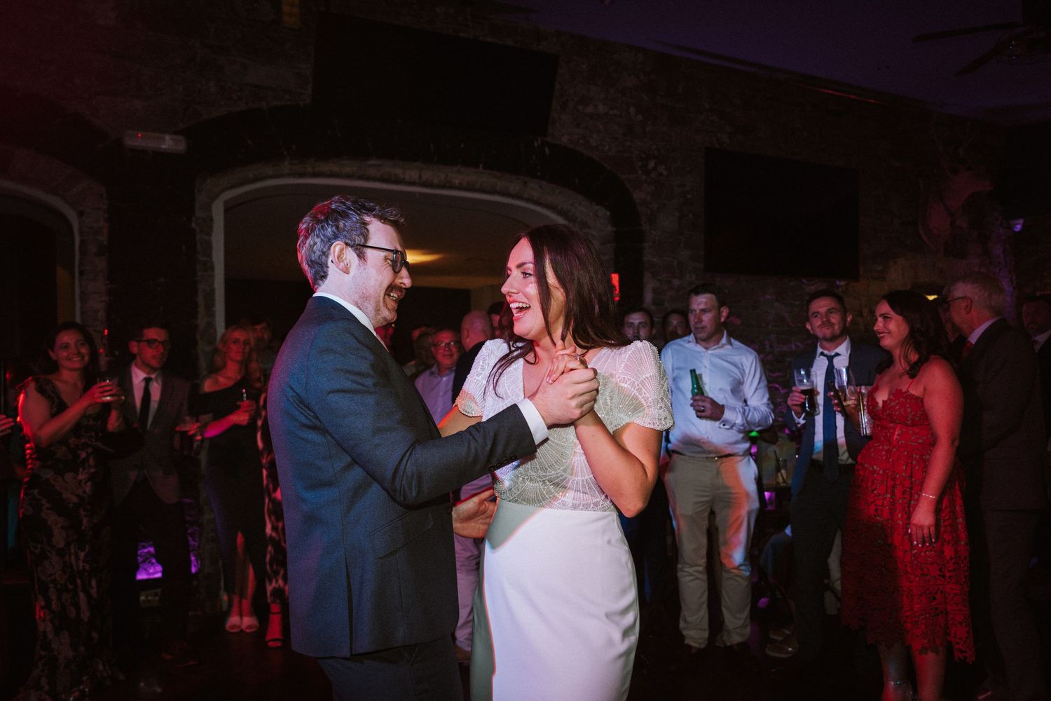 Wedding reception dance floor filled with guests dancing under moody lighting.