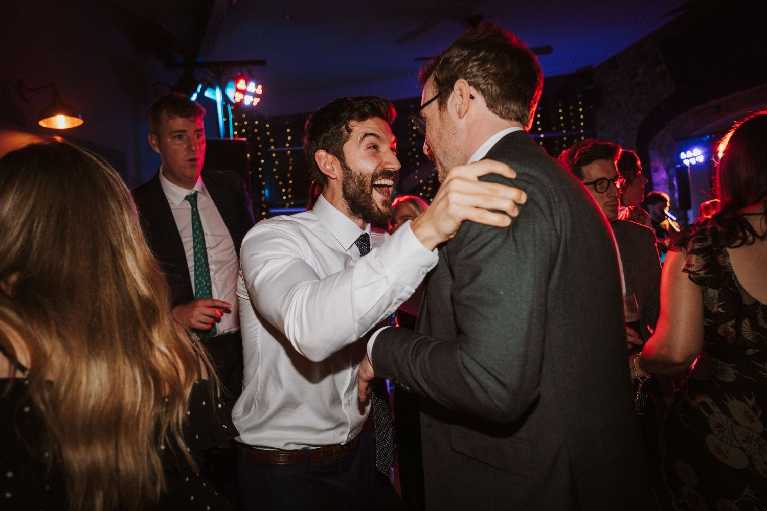 Wedding guests dance and celebrate on a dimly lit dance floor with blue lighting and festive atmosphere.