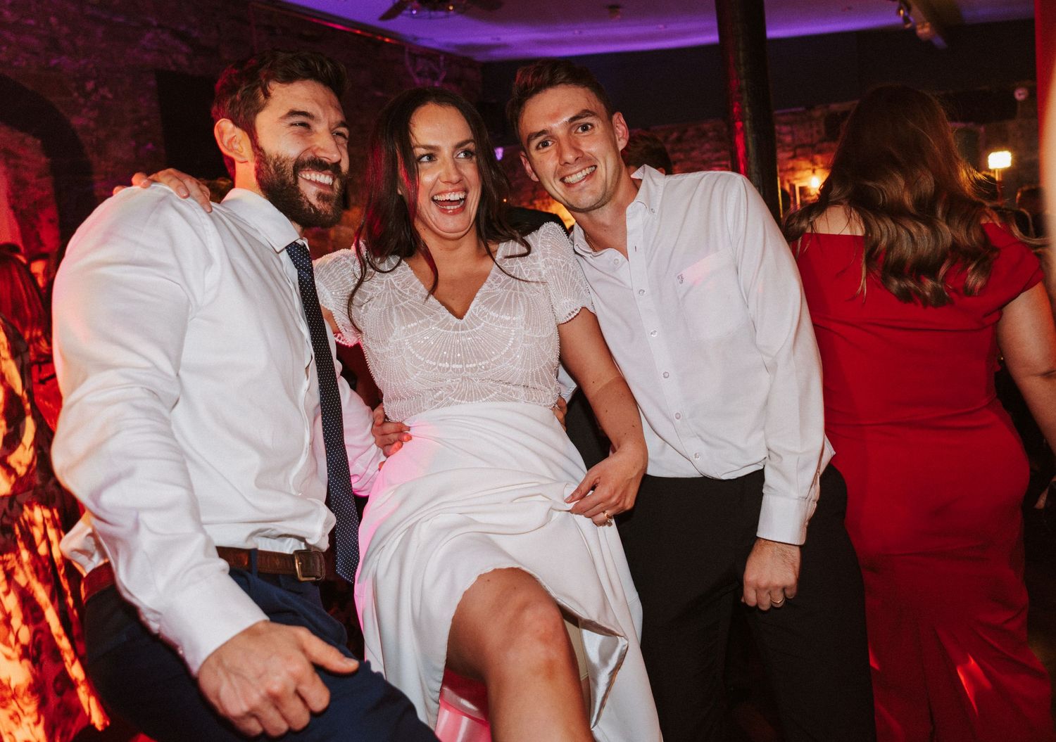 Wedding party having fun on dance floor with red lighting at reception.