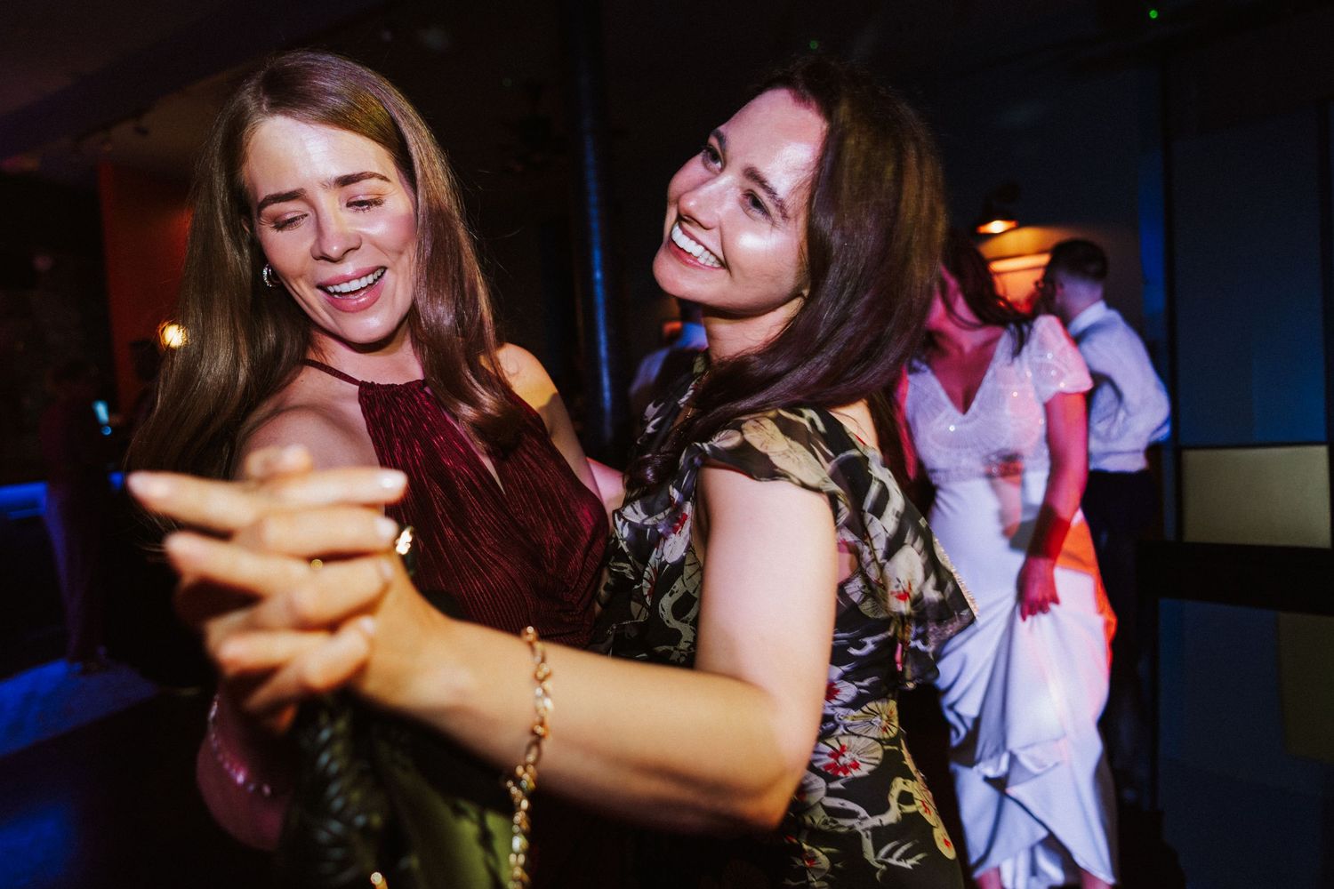 Wedding guests dancing and celebrating at a lively reception party with dark lighting and joyful atmosphere.