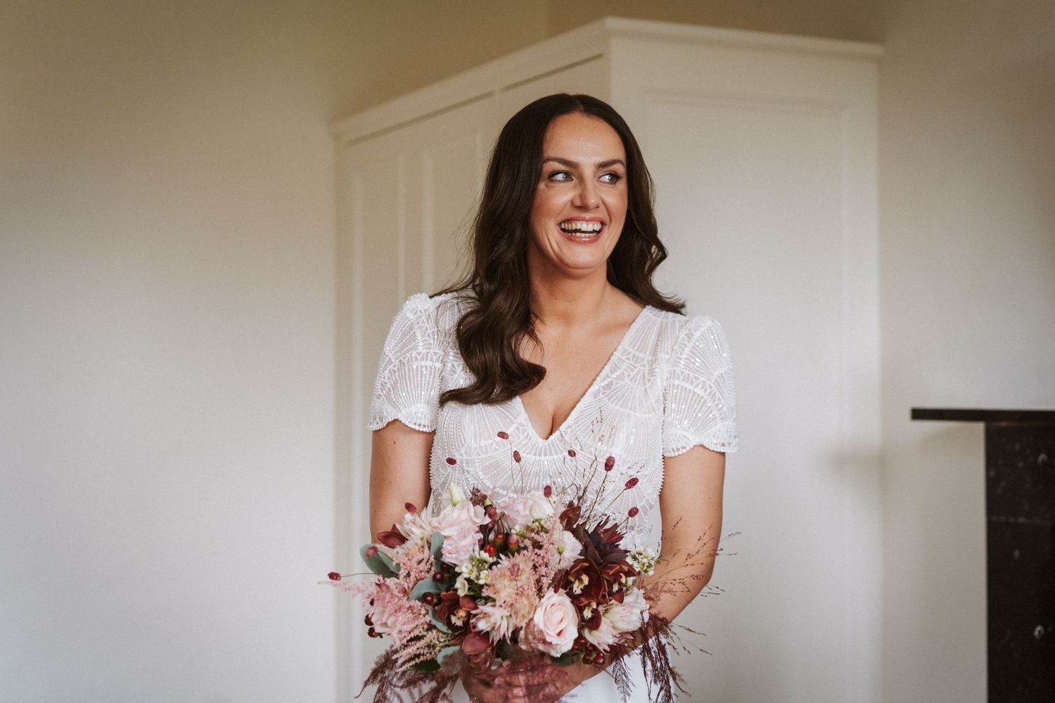 Bride holding beautiful pink and white bouquet while standing in front of white wall.