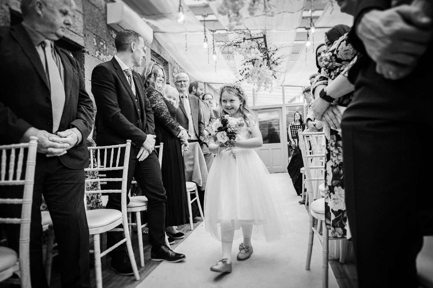 Wedding ceremony guests seated in white chairs during an indoor celebration.