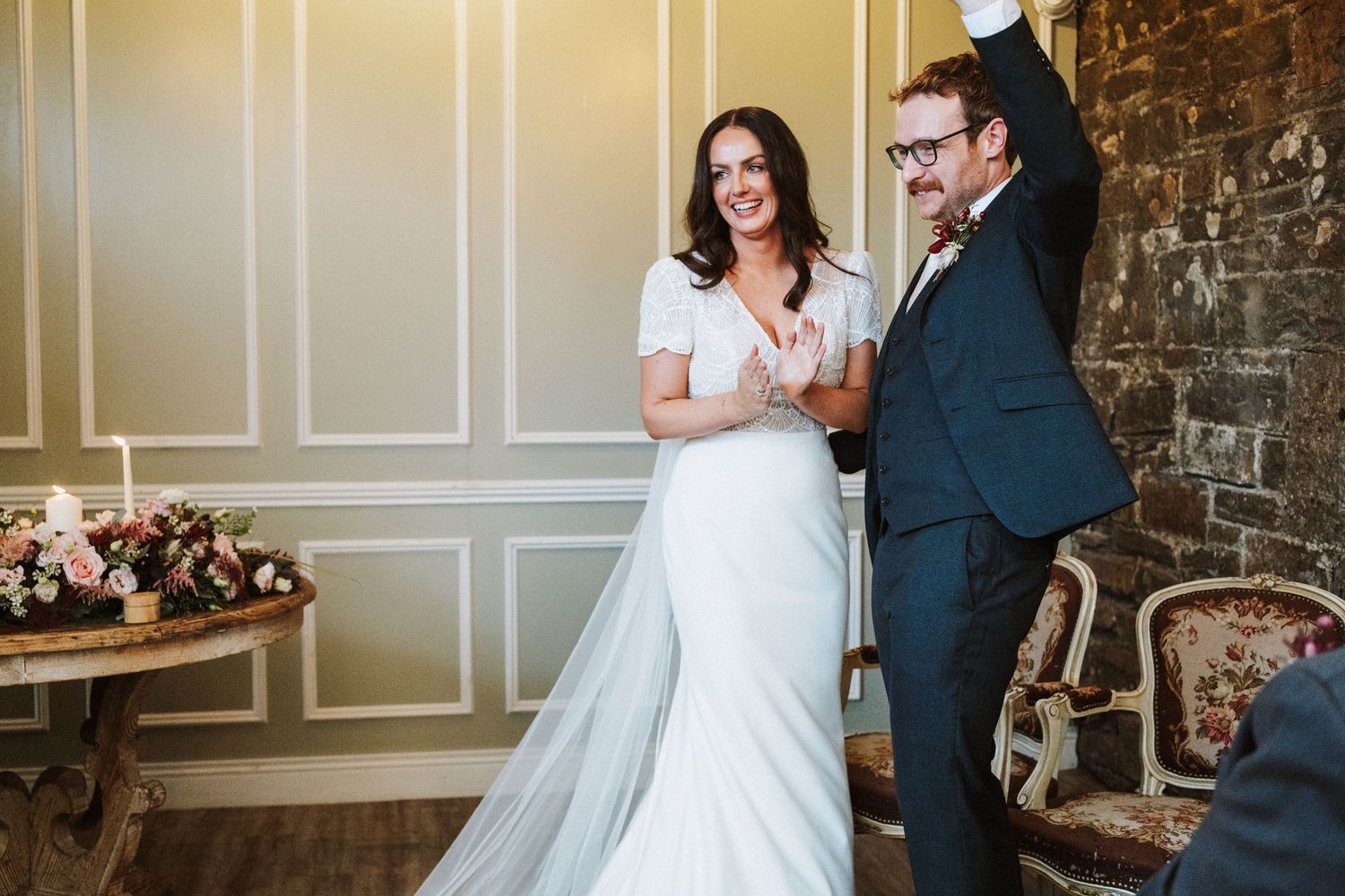 Elegant wedding couple poses against textured wall with classic architectural details.