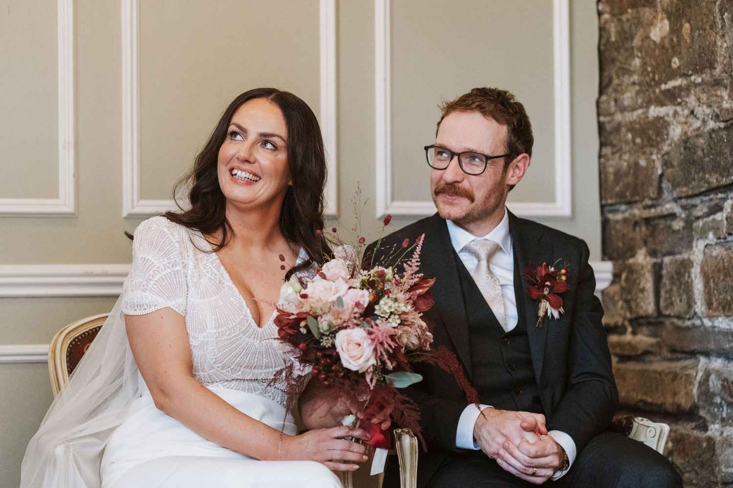 Wedding couple sitting together in an elegant room with stone walls and classic decor.