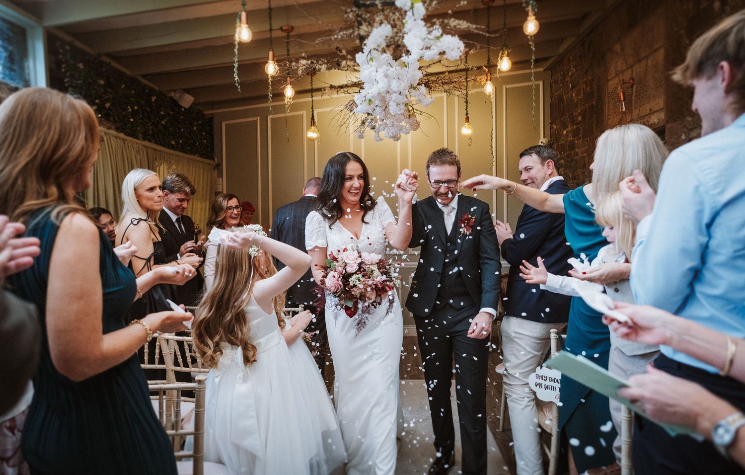 Wedding party celebrates in an elegant ballroom with chandelier and confetti.