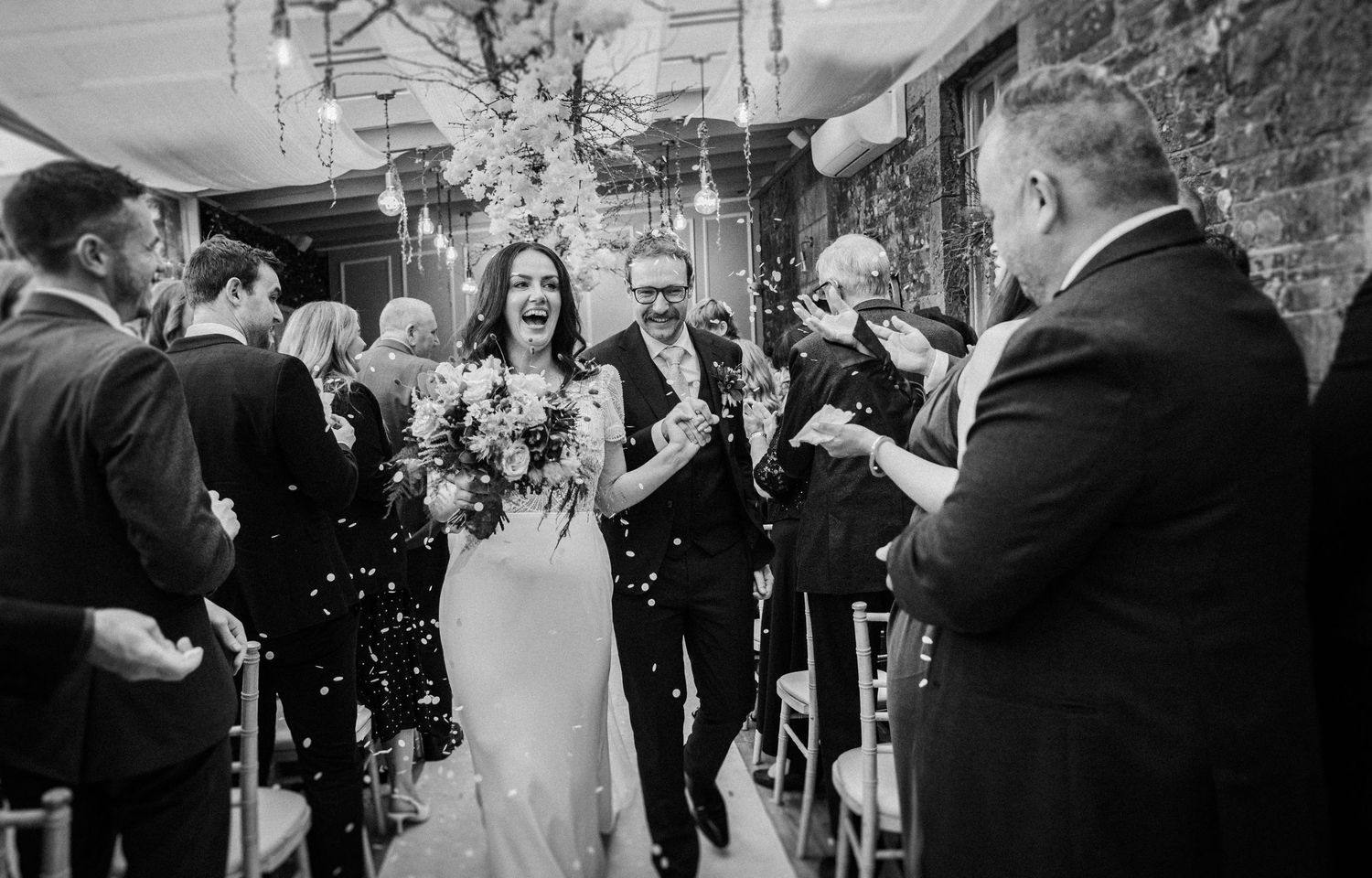 Wedding guests celebrate on a dance floor with confetti and joyful energy in black and white.