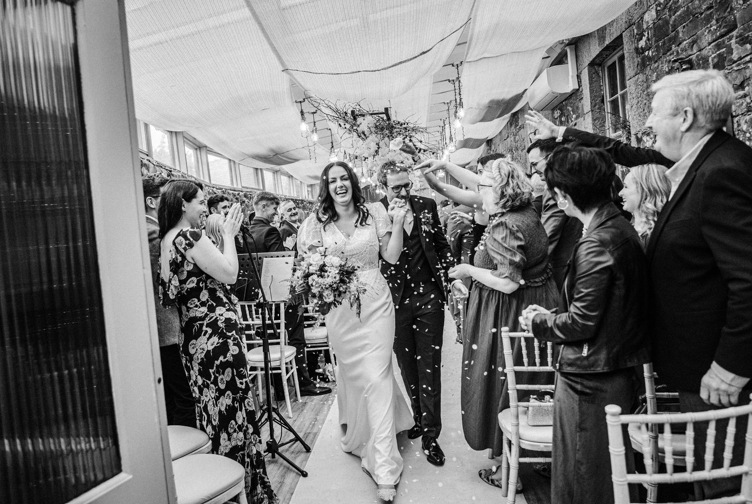 Wedding party dancing and celebrating in a venue with white chairs and festive atmosphere.