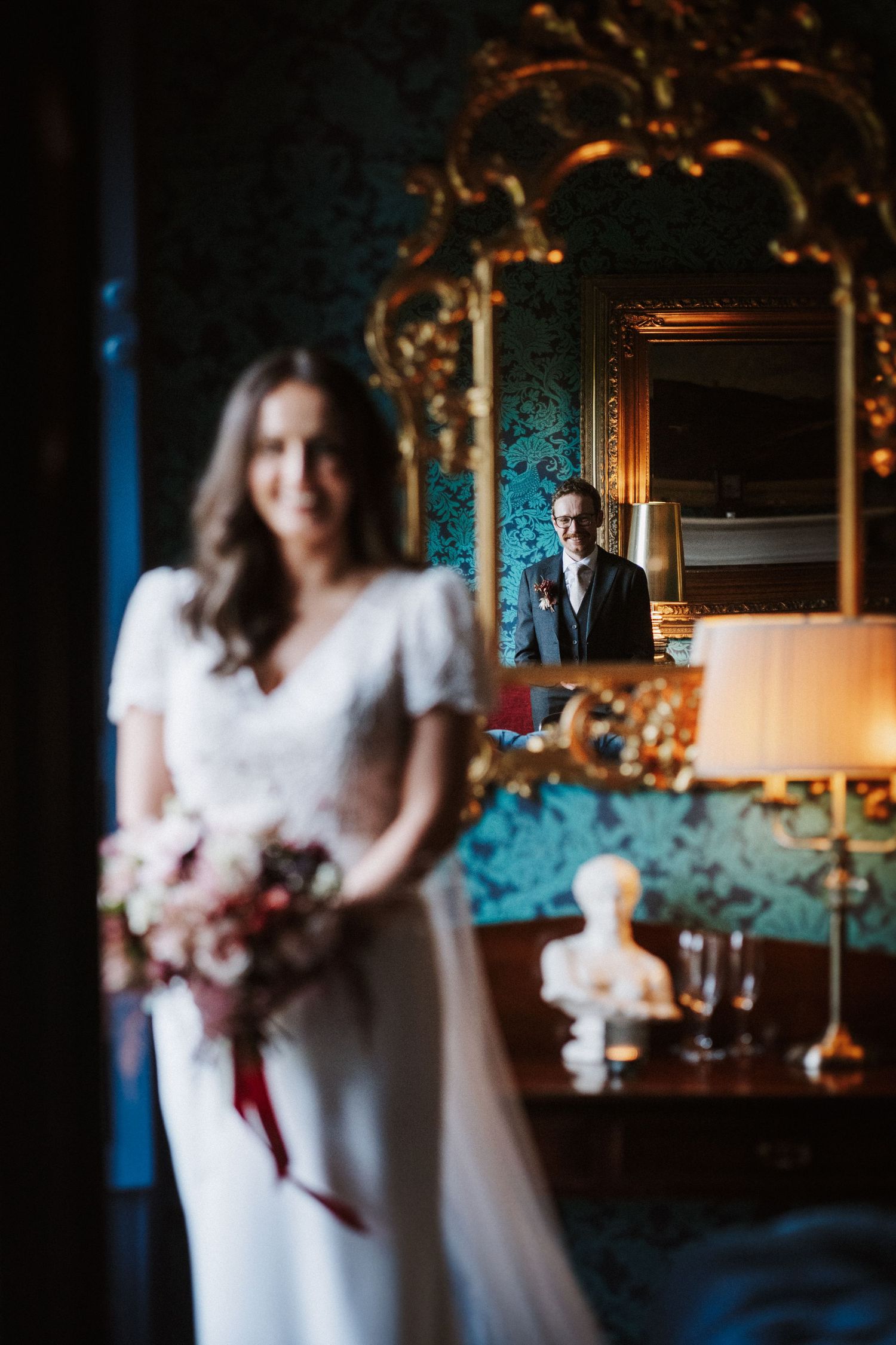 A romantic scene with two figures in white dresses standing close together in an elegant room with ornate decor and lighting.