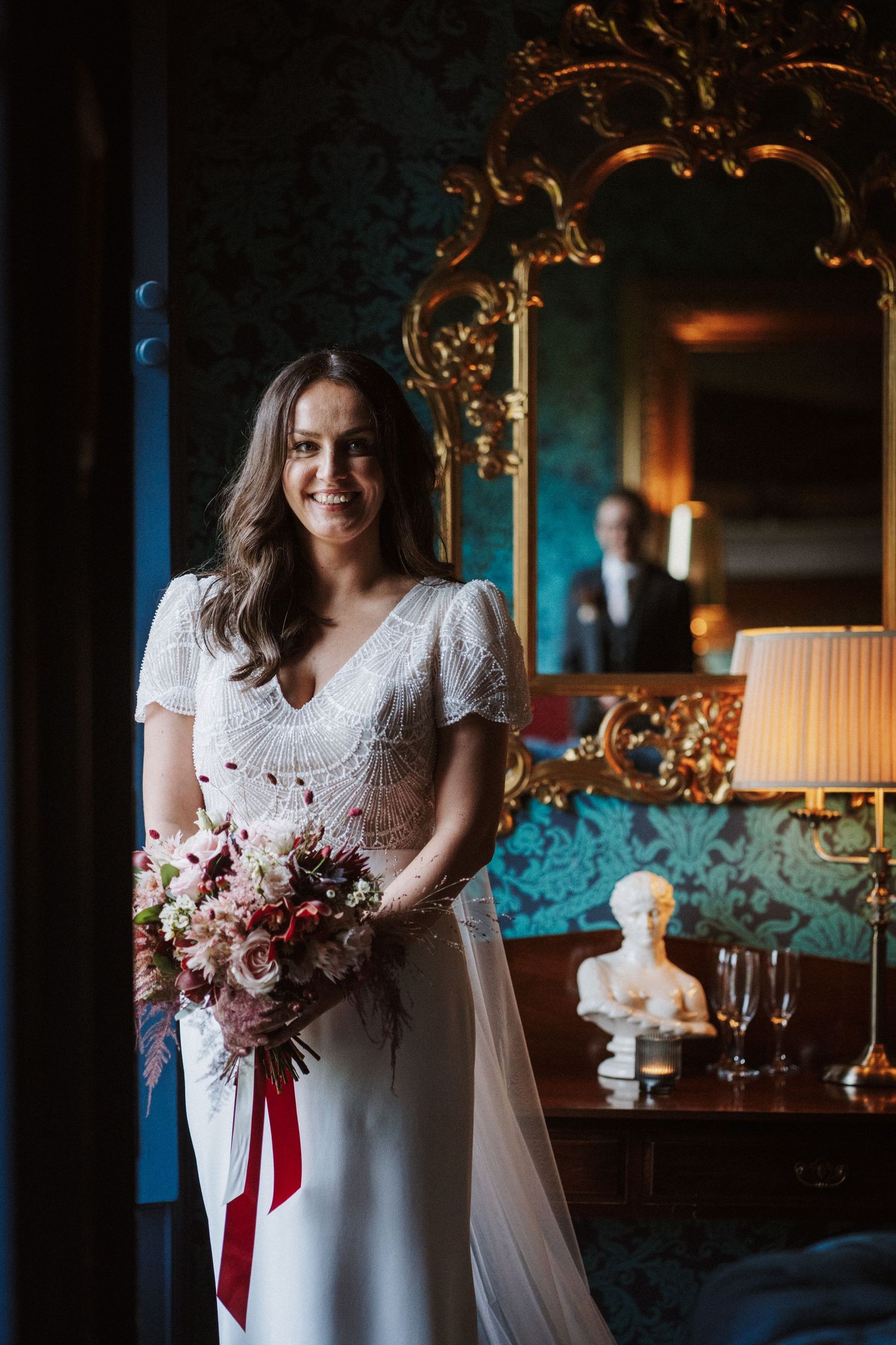 Moody wedding photography series featuring a white dress and burgundy bouquet in a dimly lit vintage room.