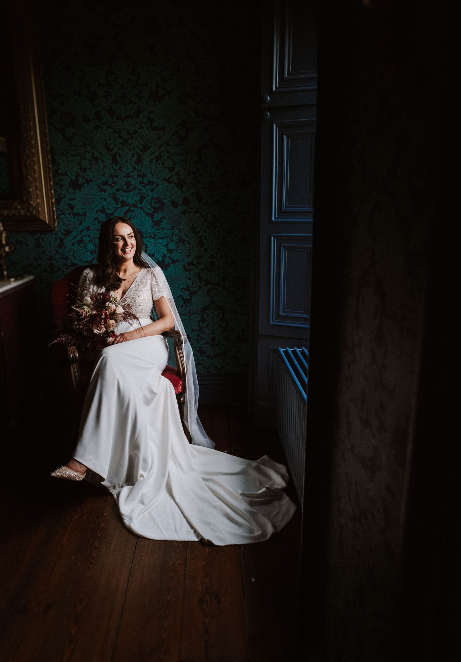 Dramatic low-light portrait of someone in a white wedding dress seated in a dark room.