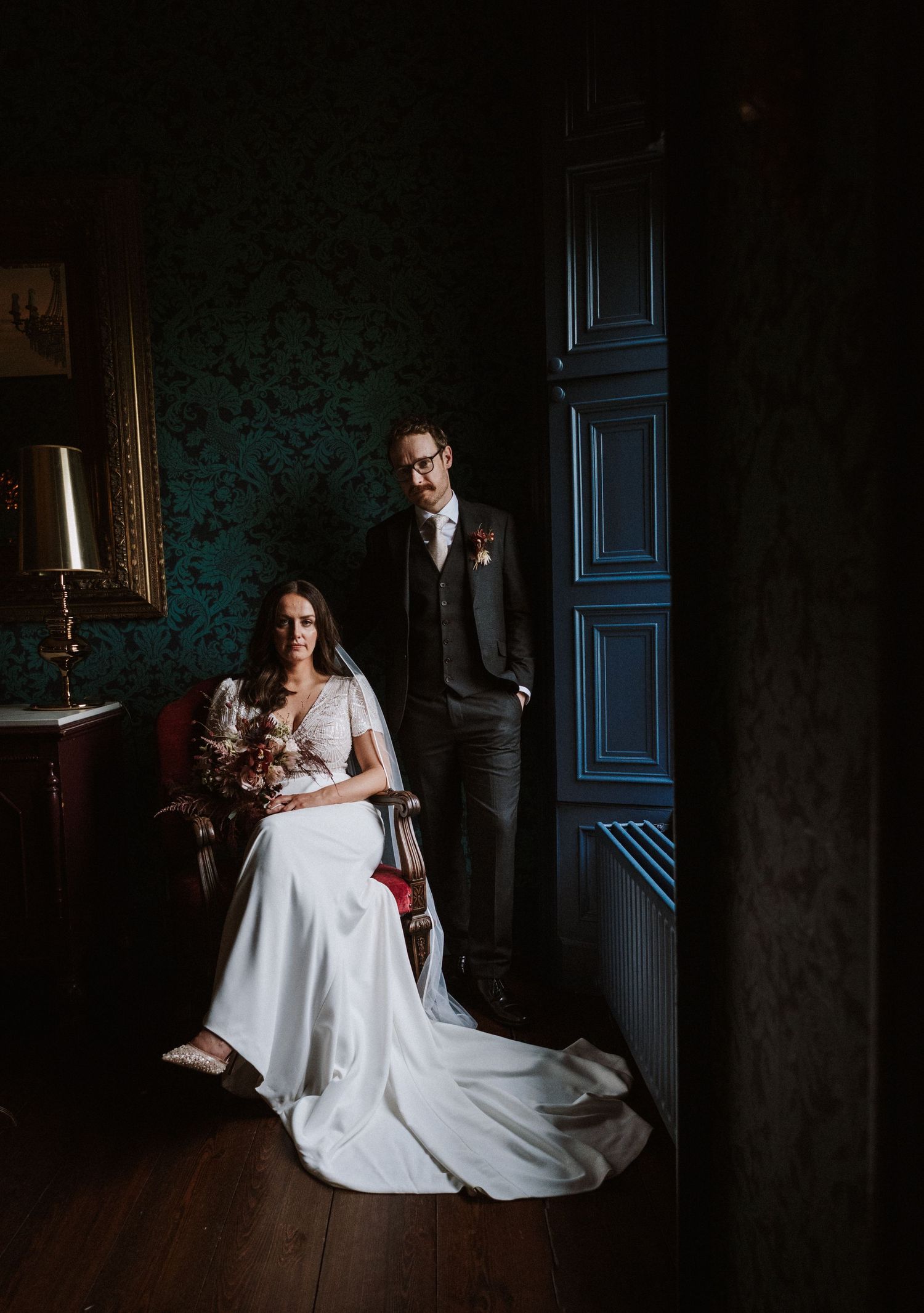 Moody bridal portrait in dark room with blue door and vintage wallpaper.