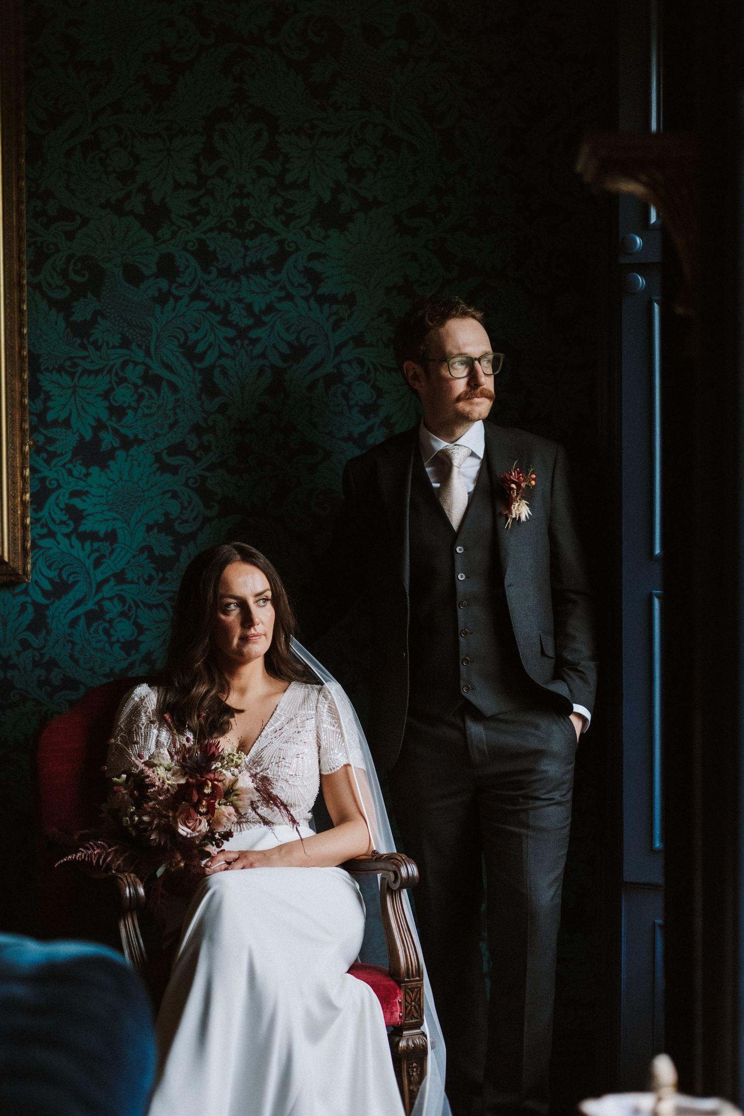 Elegant wedding scene in a dark room with dramatic teal wallpaper and moody lighting.