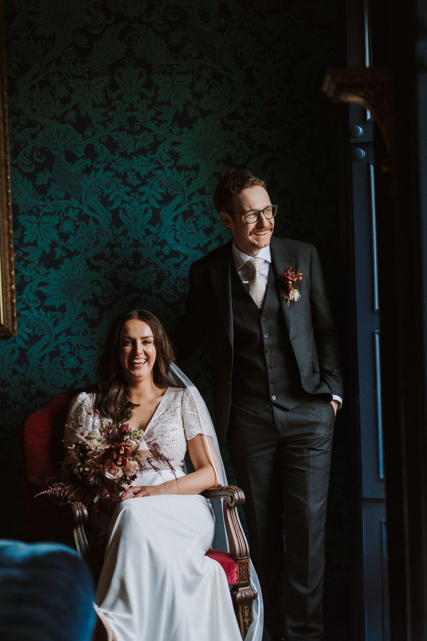 Wedding couple shares intimate moment in room with teal damask wallpaper.