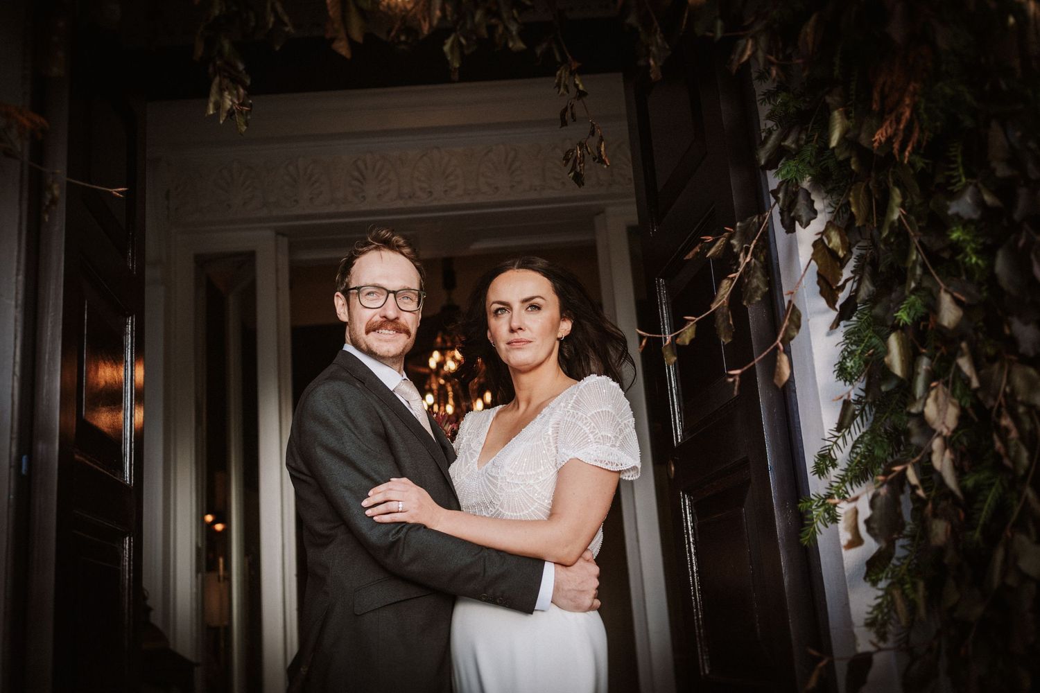 A couple shares an intimate moment during their wedding in a room decorated with climbing vines and natural light.