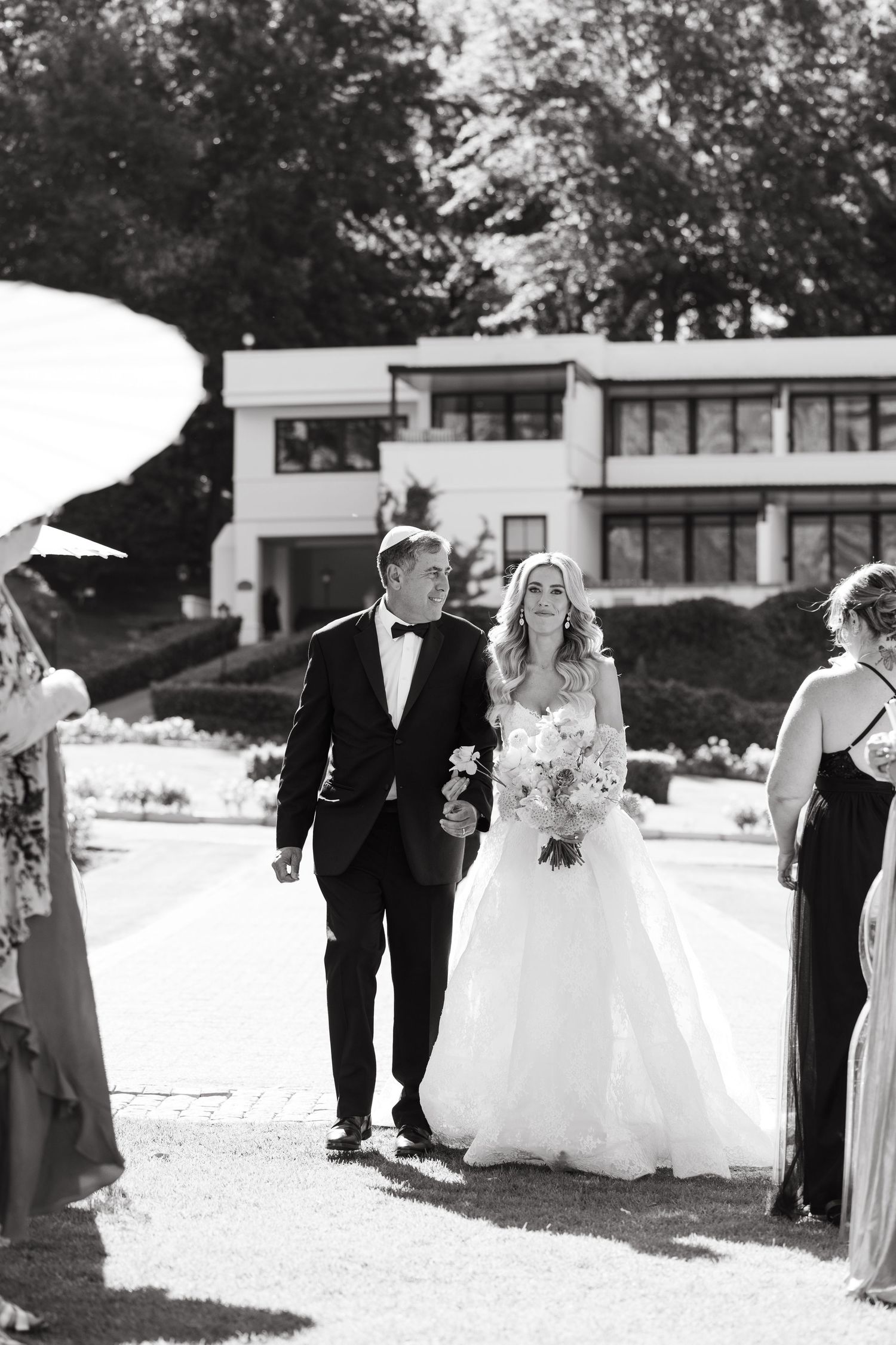A black and white photo sequence showing a wedding party walking outside on a sunny day with trees and buildings in background.