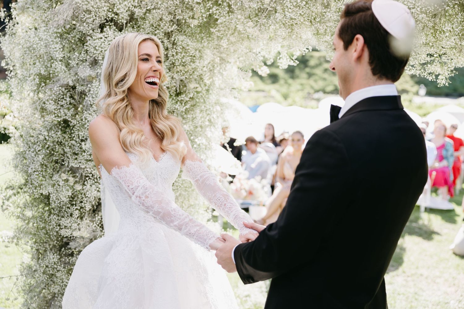 A bride and groom share a romantic moment under blooming white flowers at their outdoor wedding.
