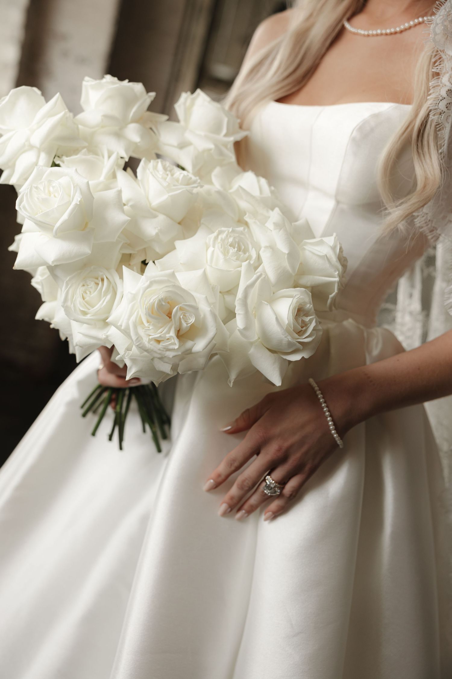Close-up view of an elegant white rose bridal bouquet held against a classic white wedding dress.