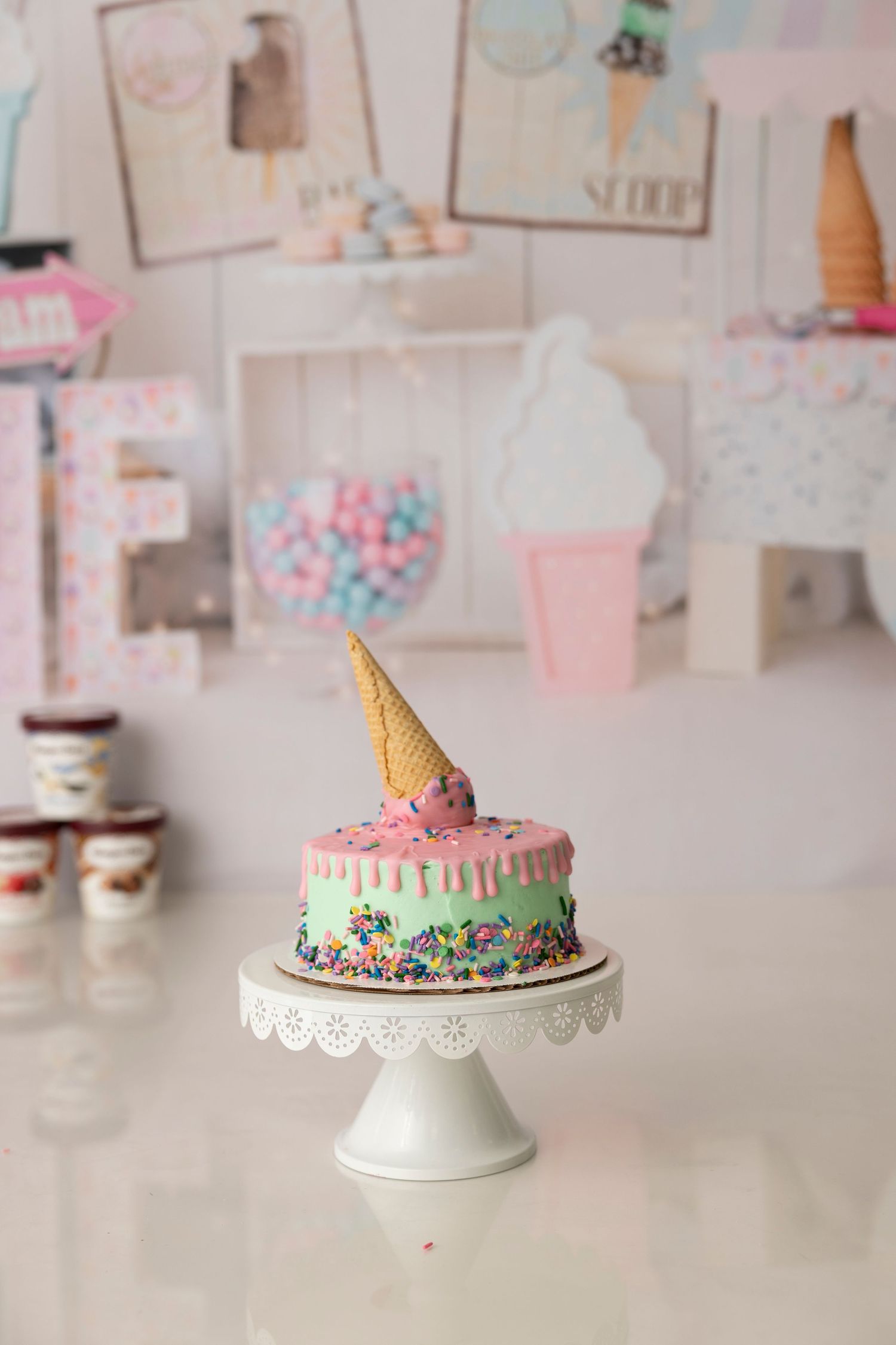 Four delicate pastel birthday cakes decorated with sprinkles and frosting displayed on white cake stands against a soft background.