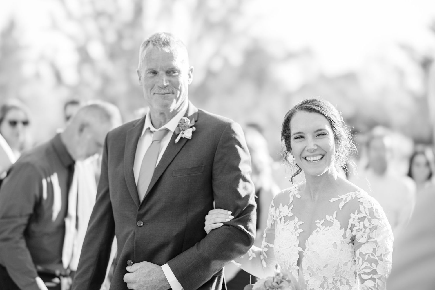 A scenic outdoor wedding ceremony with mountain views and guests seated in white chairs under green trees.