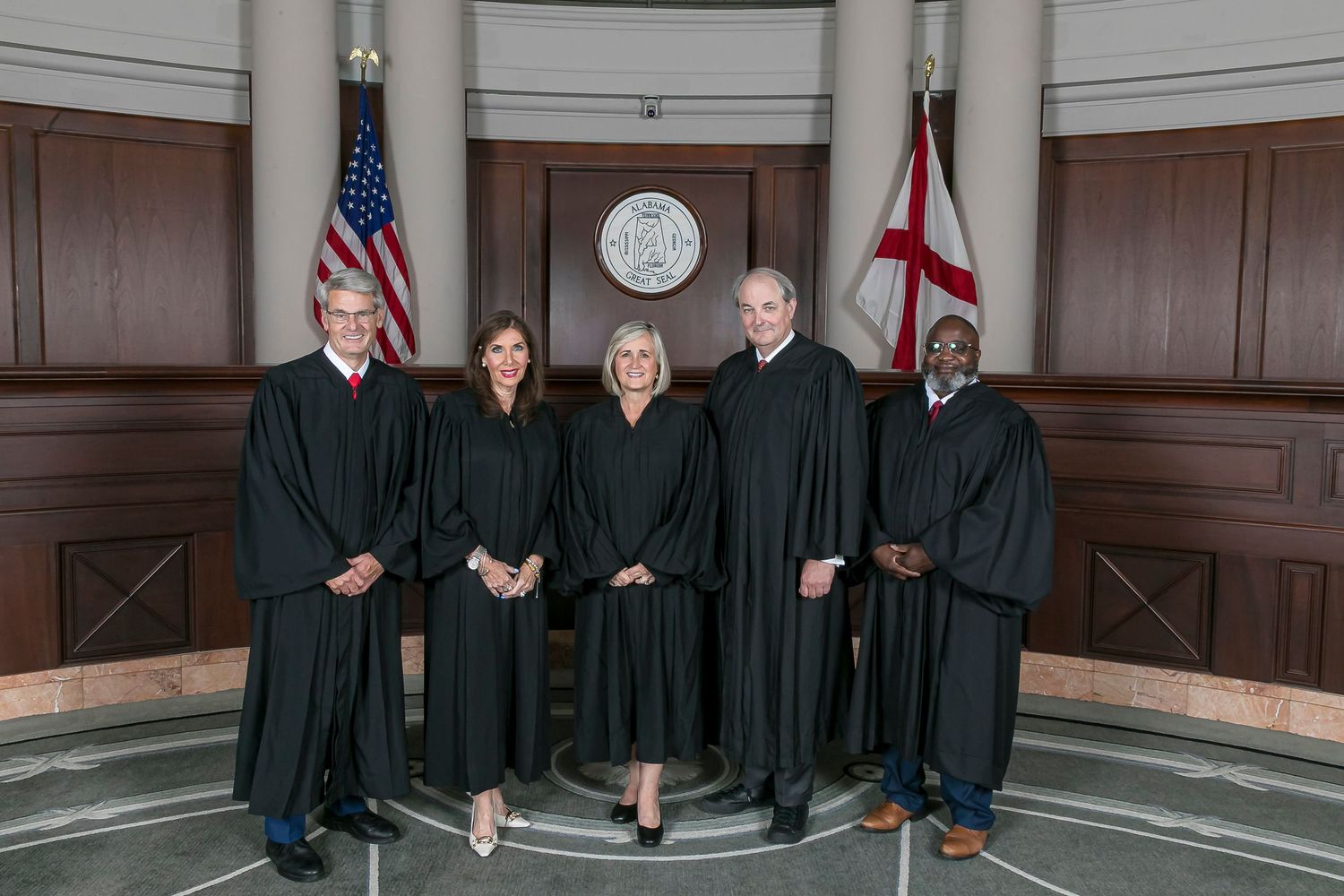Supreme Court justices in black robes stand together for a formal group photograph in a wood-paneled courtroom.