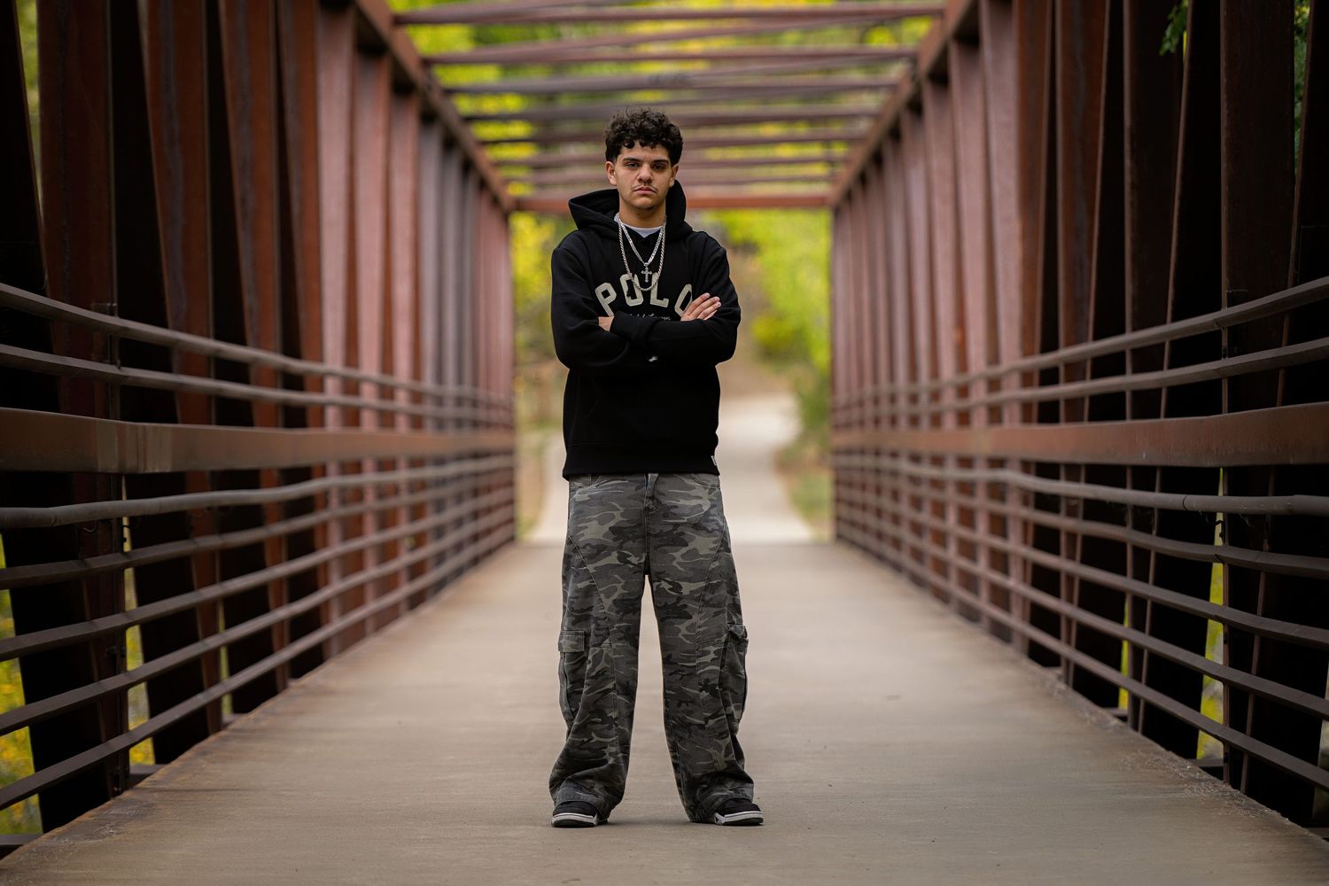 A Westminster Senior stands in the middle of a long covered walkway with yellow lighting and metal railings on both sides.