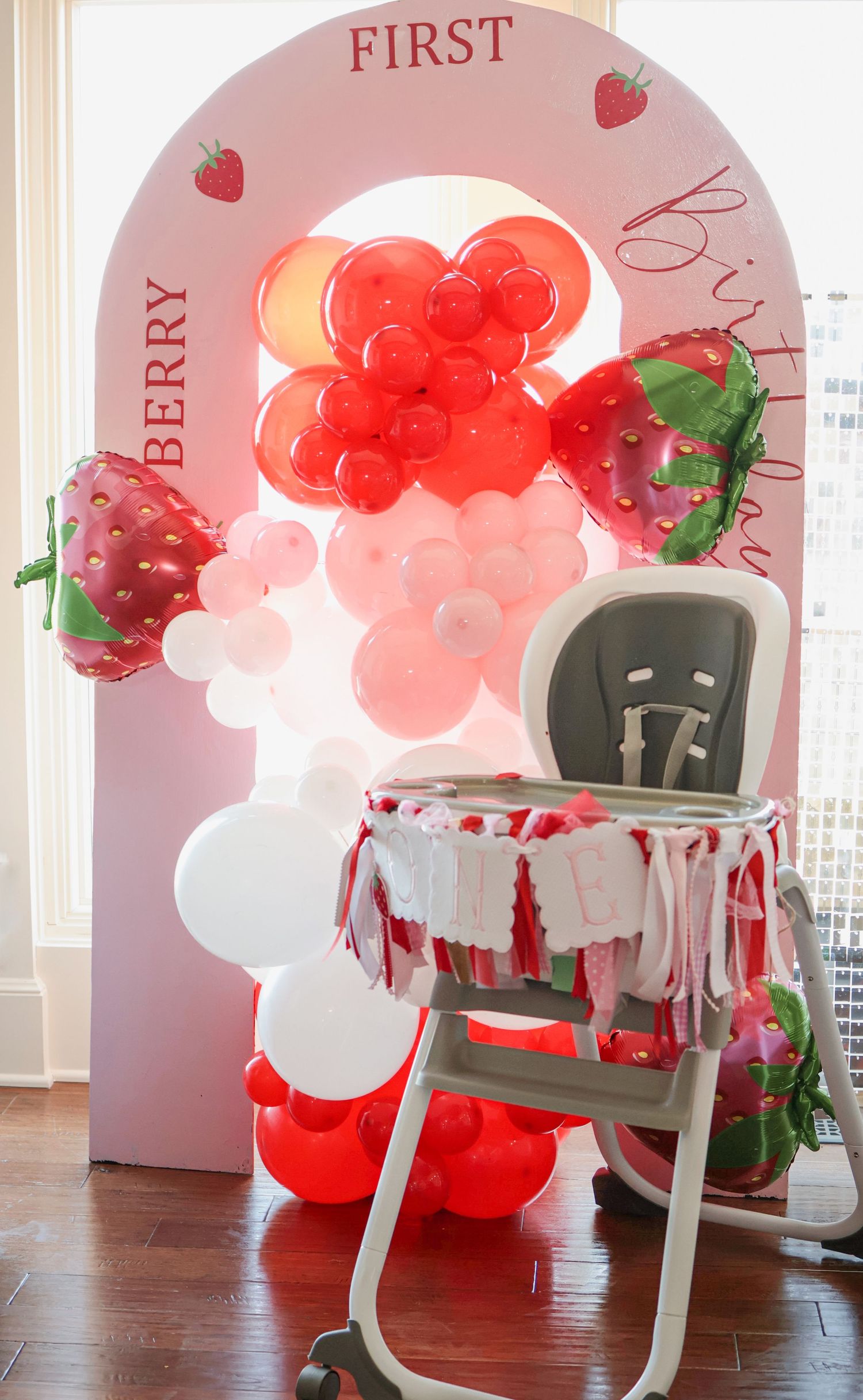 First birthday party setup with red balloon arch and strawberry theme decorations.