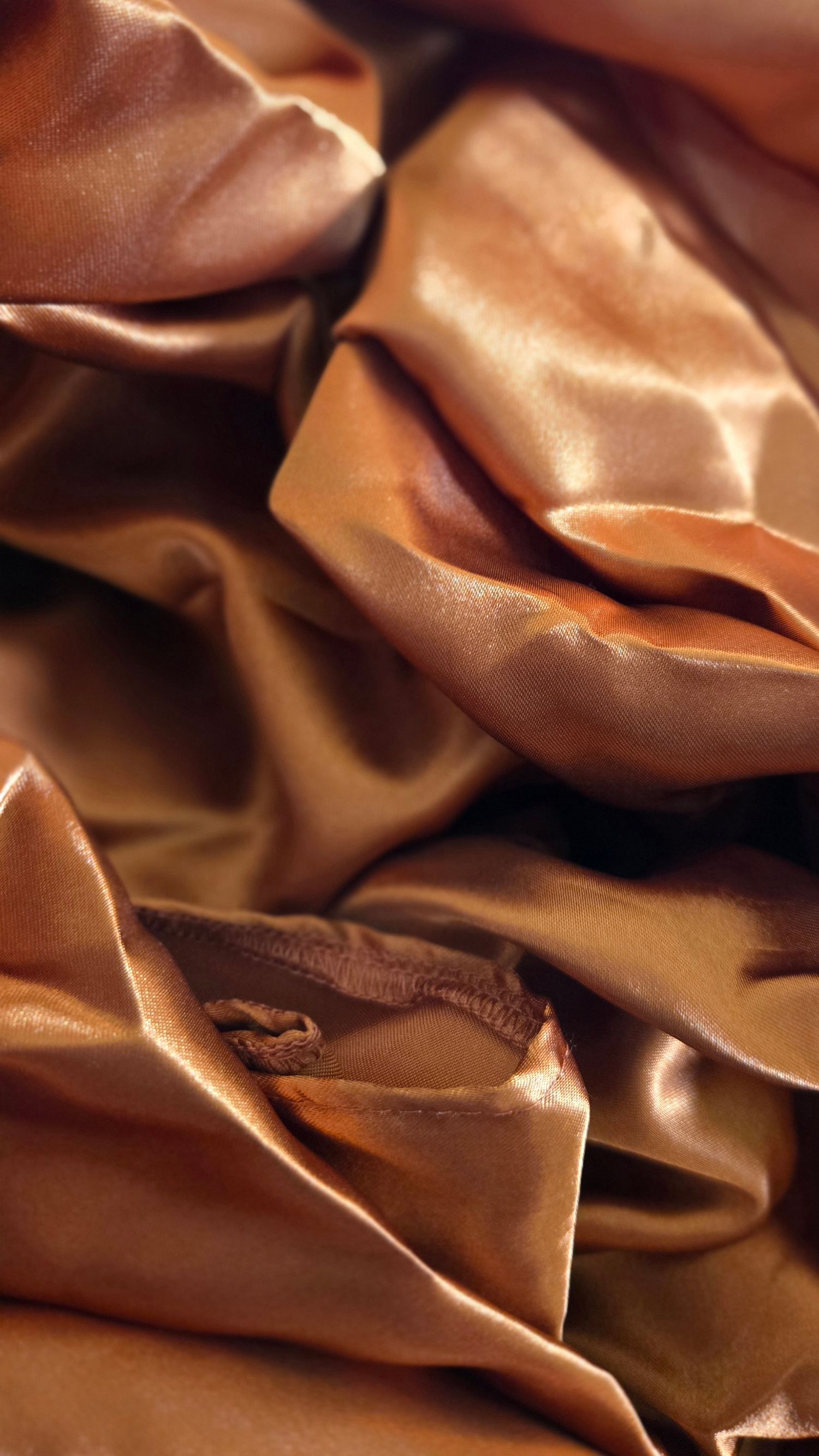 Luxurious copper-colored satin fabric with soft folds and creases creating a rich textural pattern.