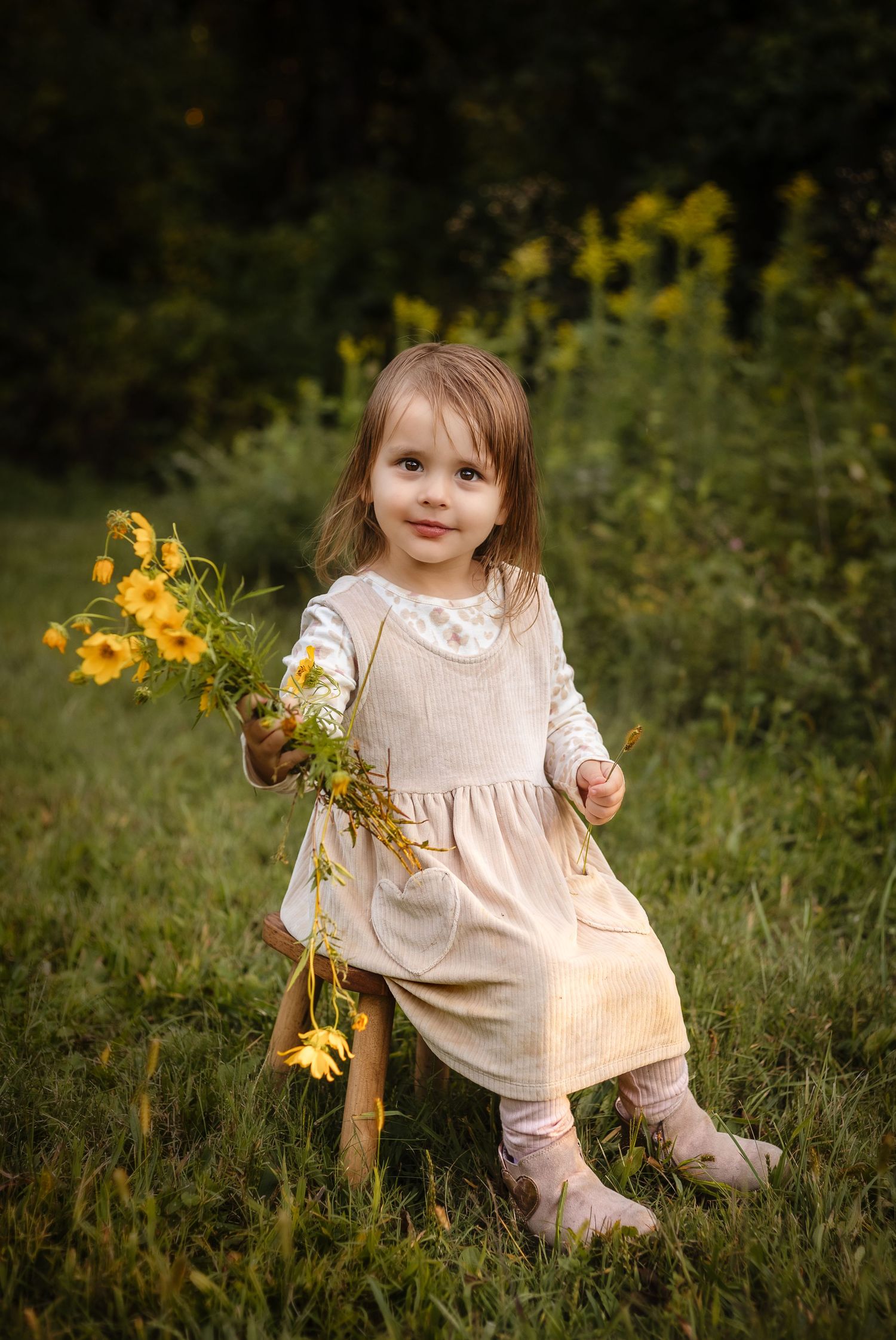 Charlottesville family photographer captures sweet three year-old girl in a blush dress and holding early fall yellow flowers.