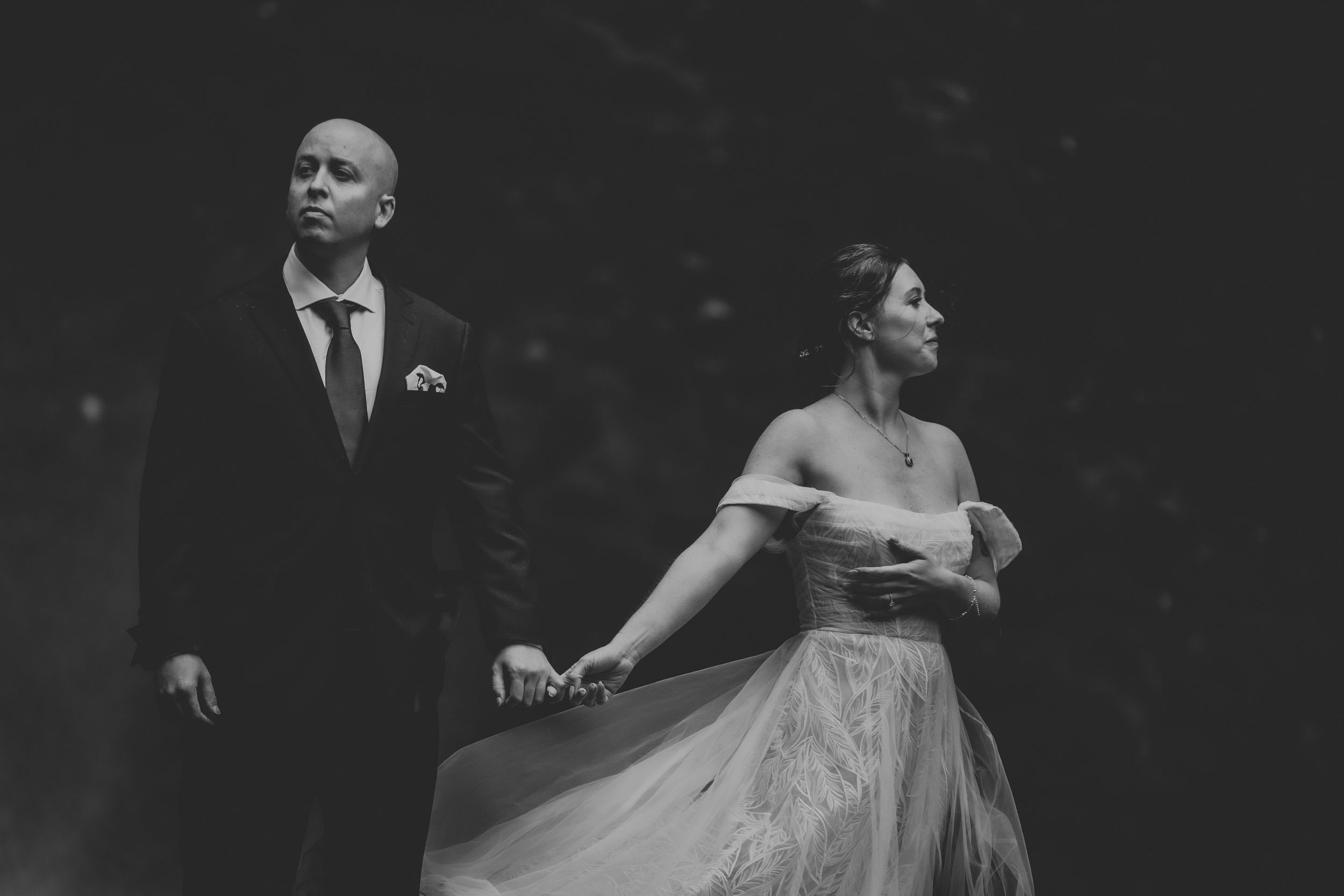 A couple shares an intimate moment in formal attire against a dark, moody background.