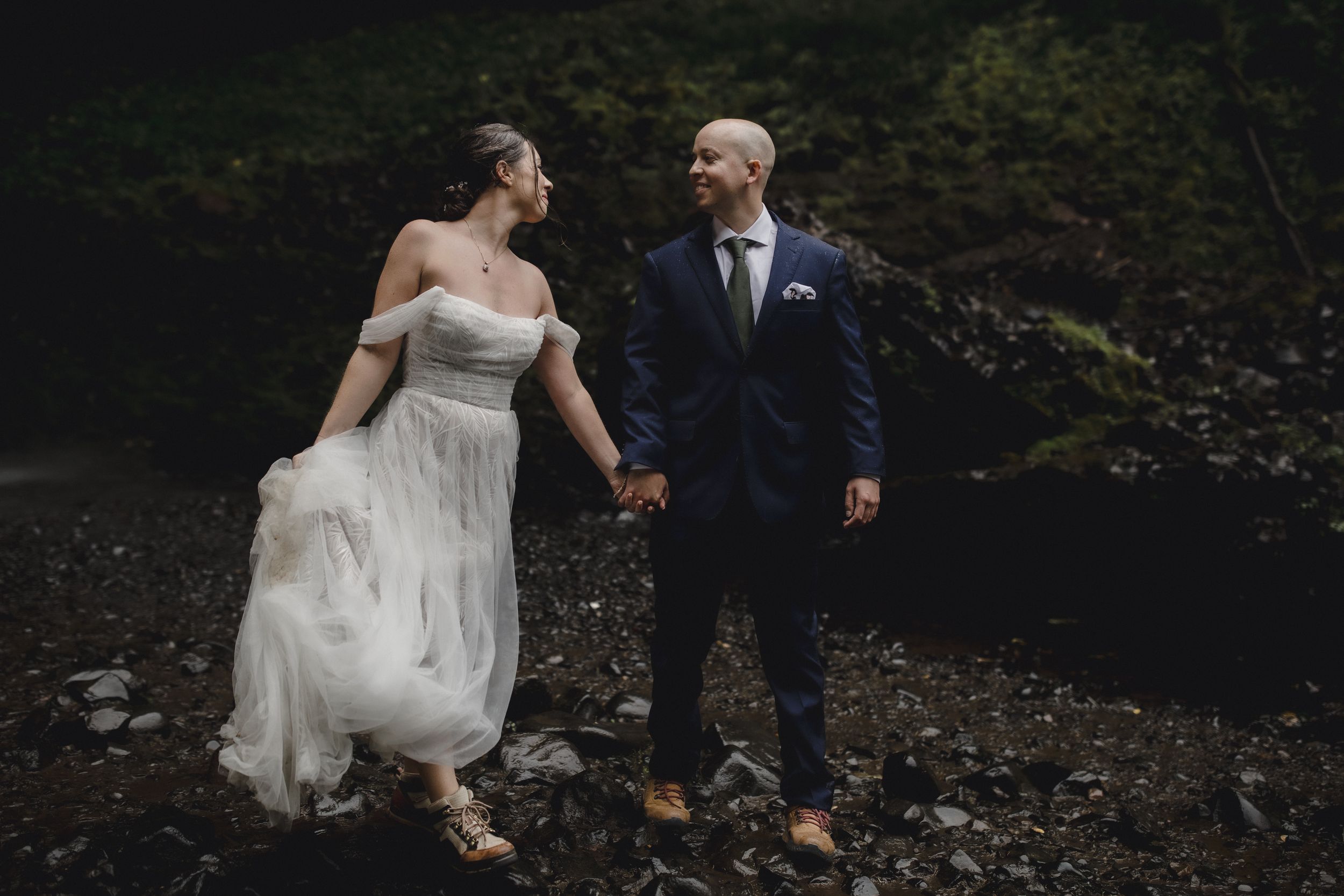 A couple shares a romantic moment on a rocky riverbank surrounded by lush forest scenery.