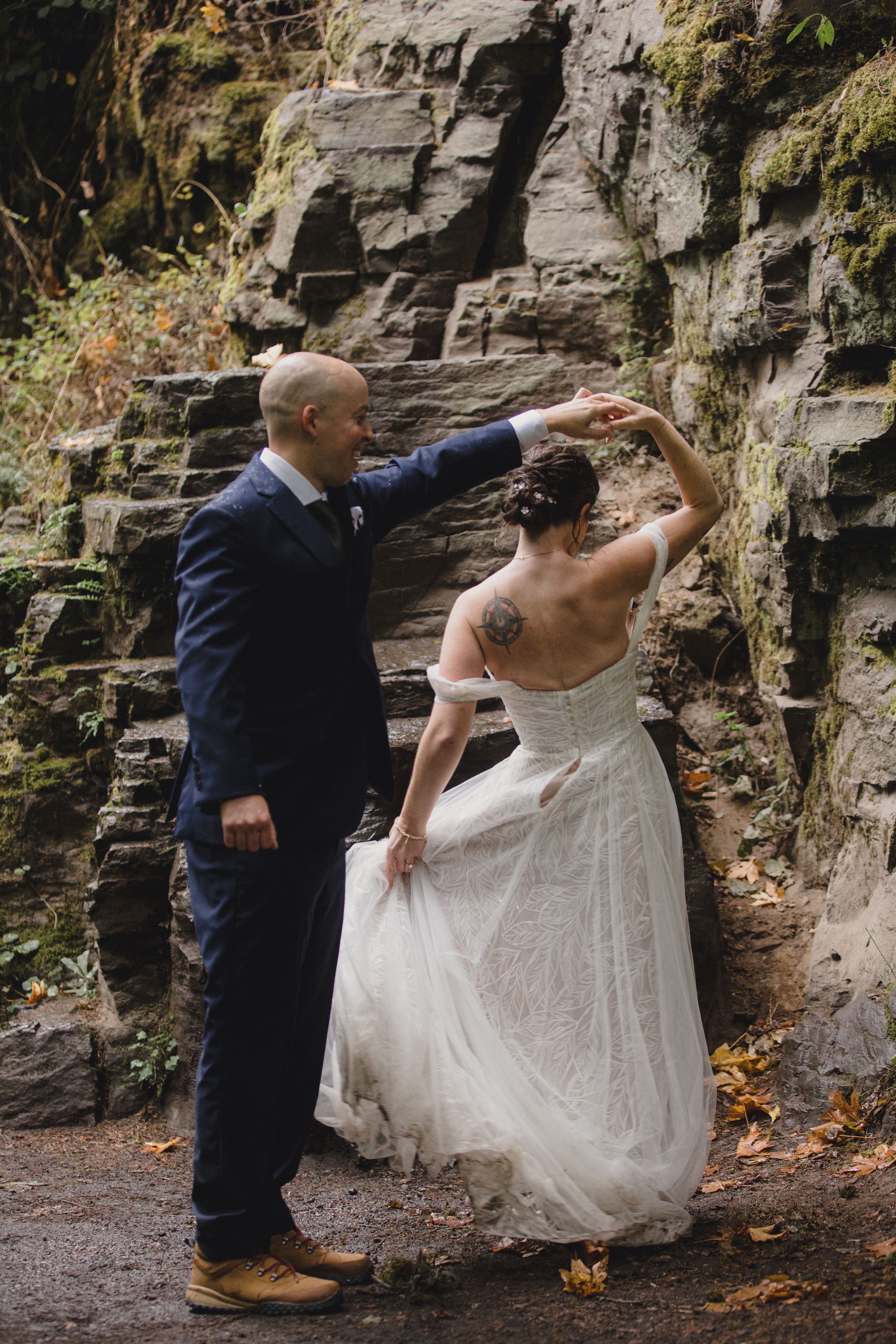 A couple in wedding attire dances playfully against a rocky cliff wall backdrop during their outdoor celebration.
