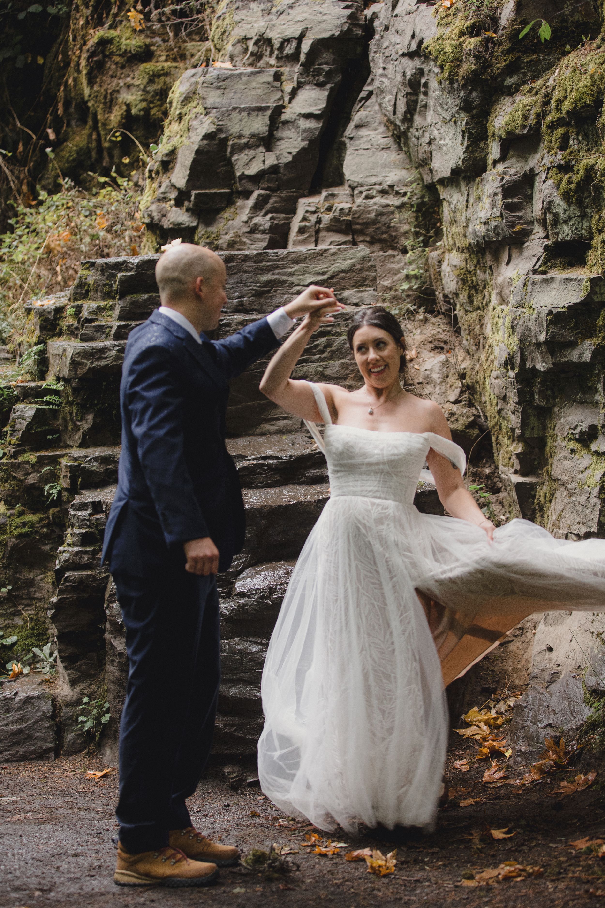 A couple dances together in front of a rocky cliff wall during an outdoor wedding photoshoot.