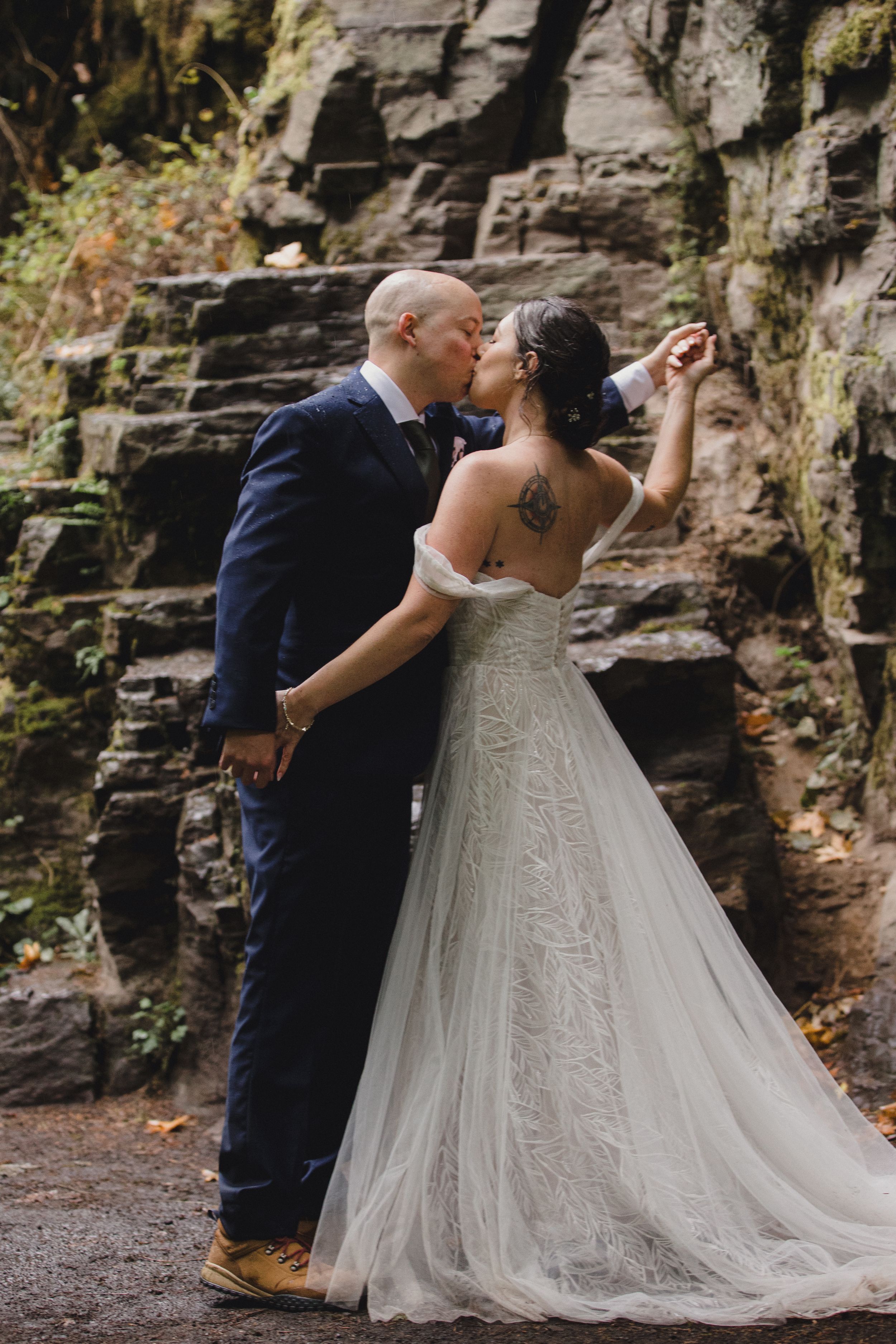 A couple shares an intimate moment against a rocky cliff wall during their wedding photoshoot.