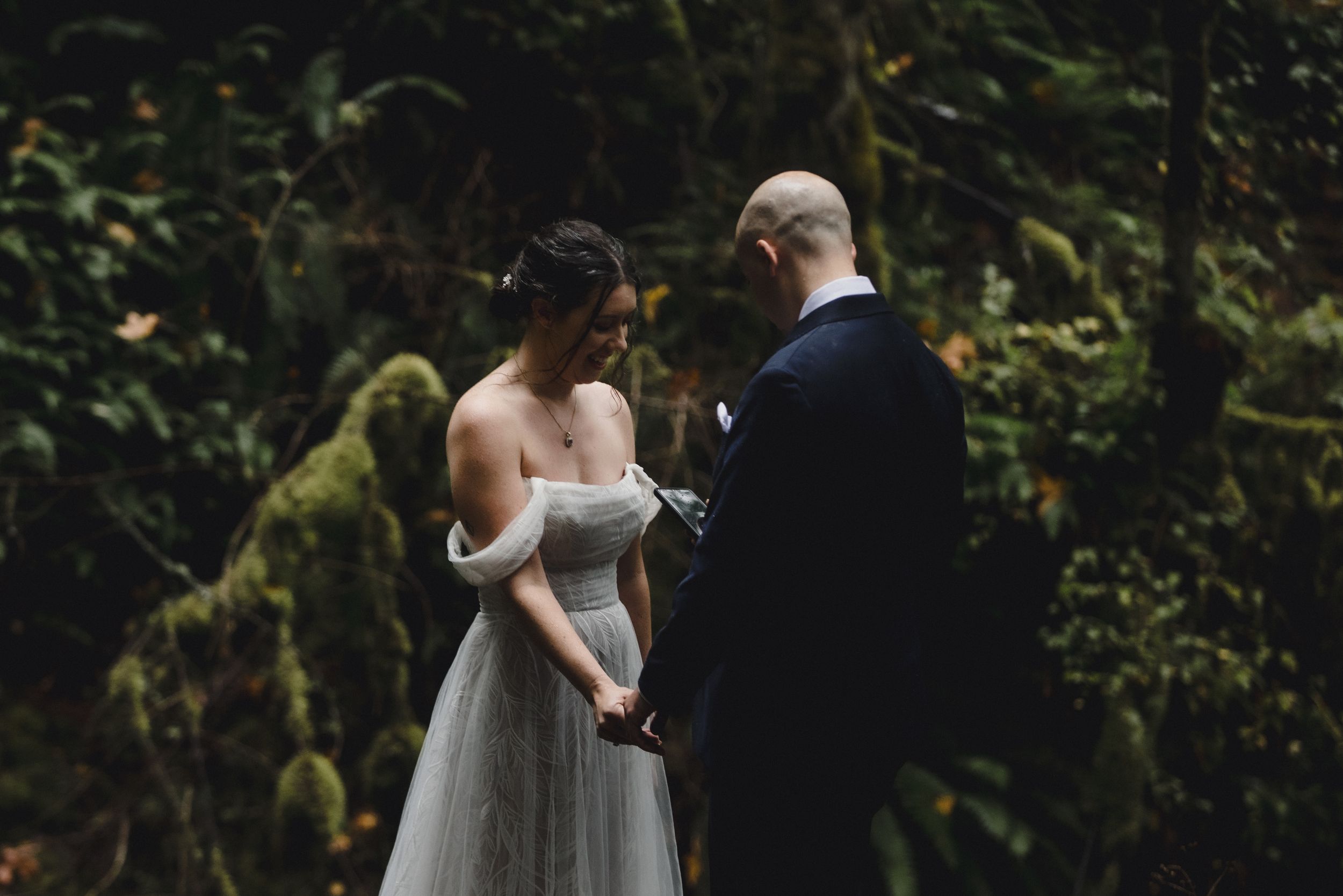 Wedding couple walks together through a moody forest setting with dramatic lighting.