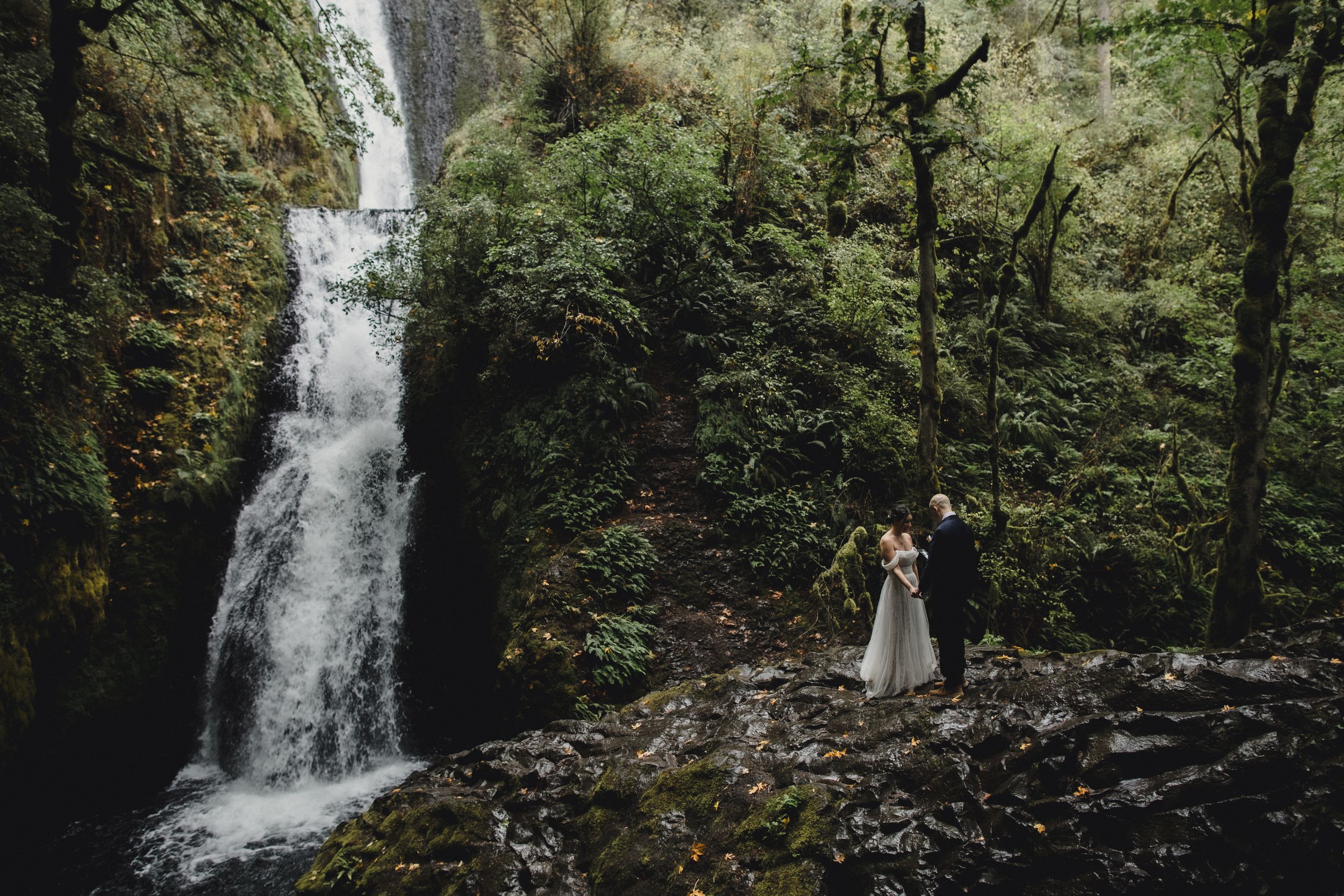 Scenic waterfall flows through green forest creating perfect backdrop for outdoor wedding photography.