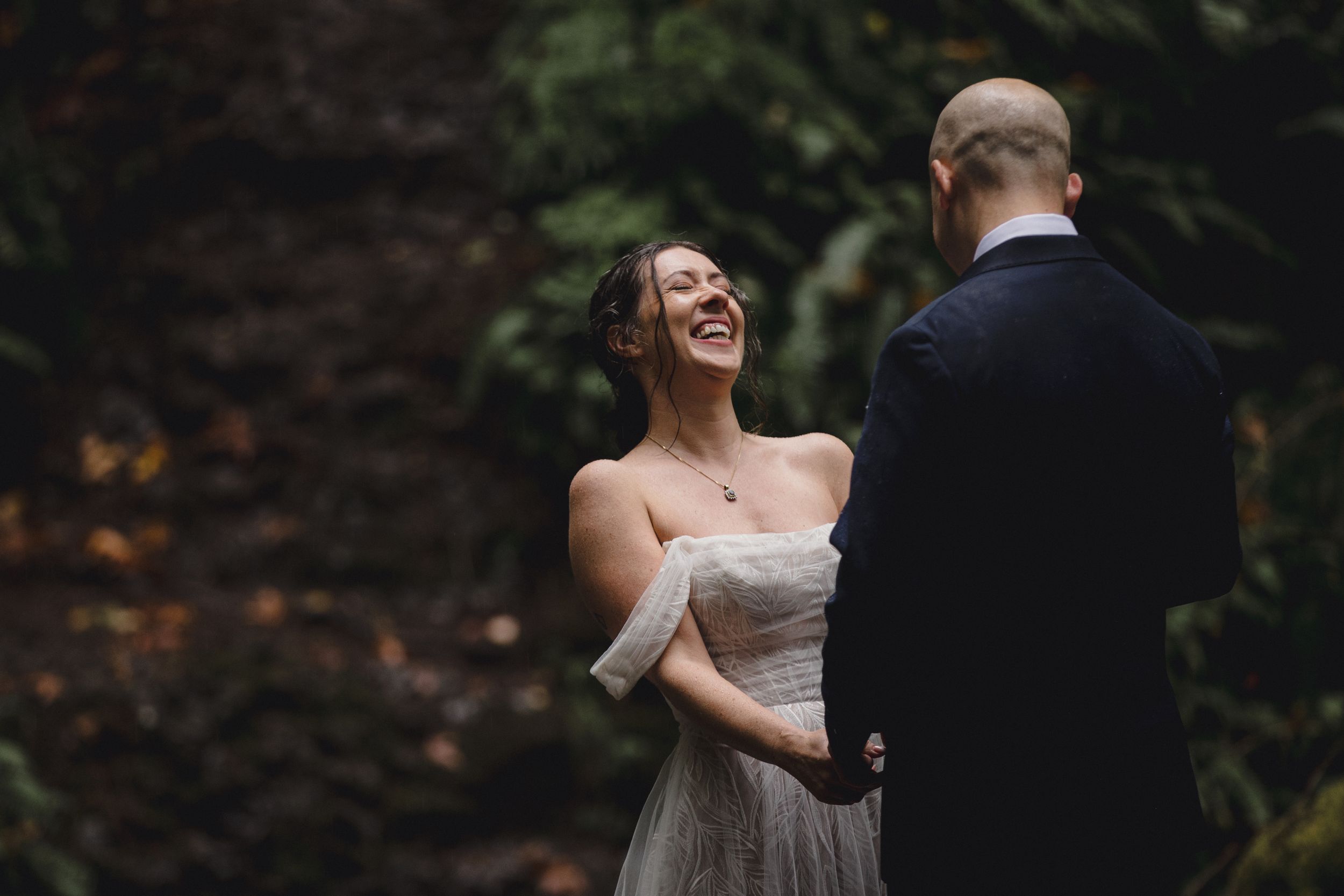 Newlyweds share a joyful moment while walking along a wooded path.