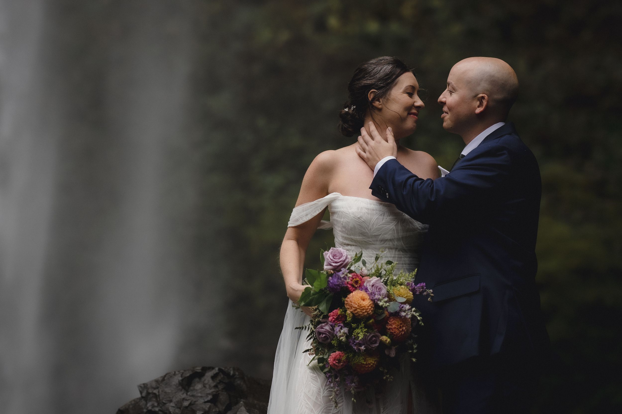 A couple shares an intimate moment during their wedding ceremony surrounded by lush greenery and colorful floral bouquets.