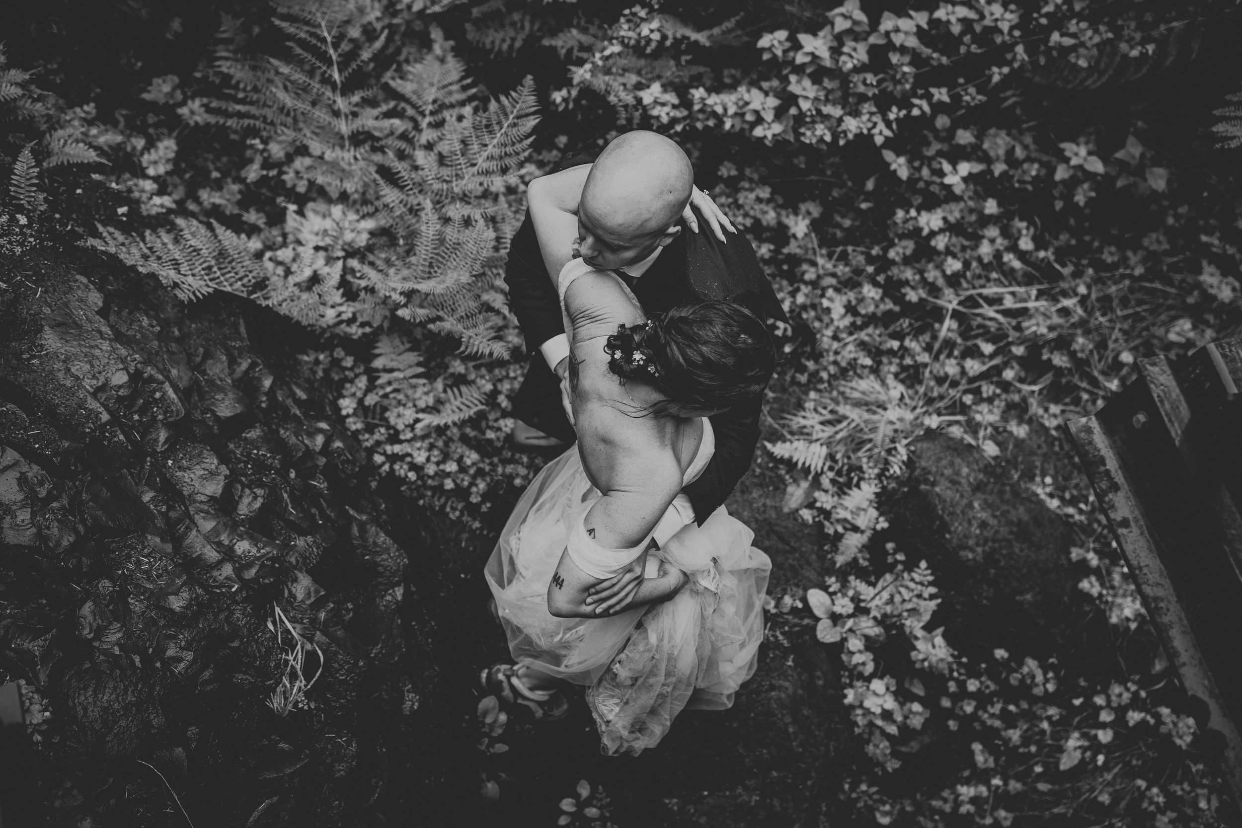 Wedding couple stands on mossy rocks near a cascading waterfall with dark moody lighting.