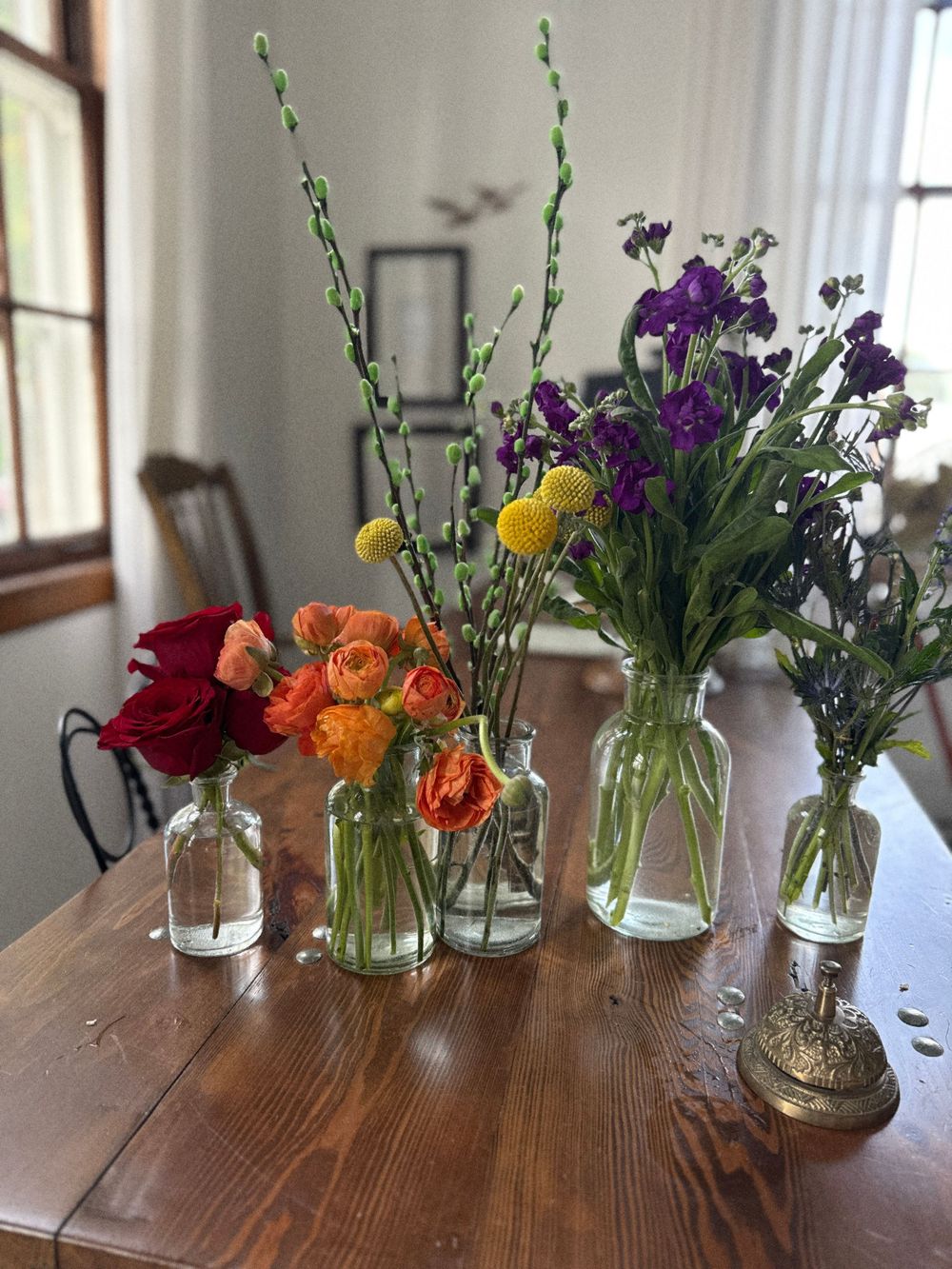 Colorful flower arrangements in clear glass vases on a wooden table, featuring red, orange, yellow, and purple blooms.