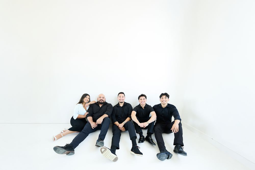 Group of people in black clothing sitting on a white floor in various poses.