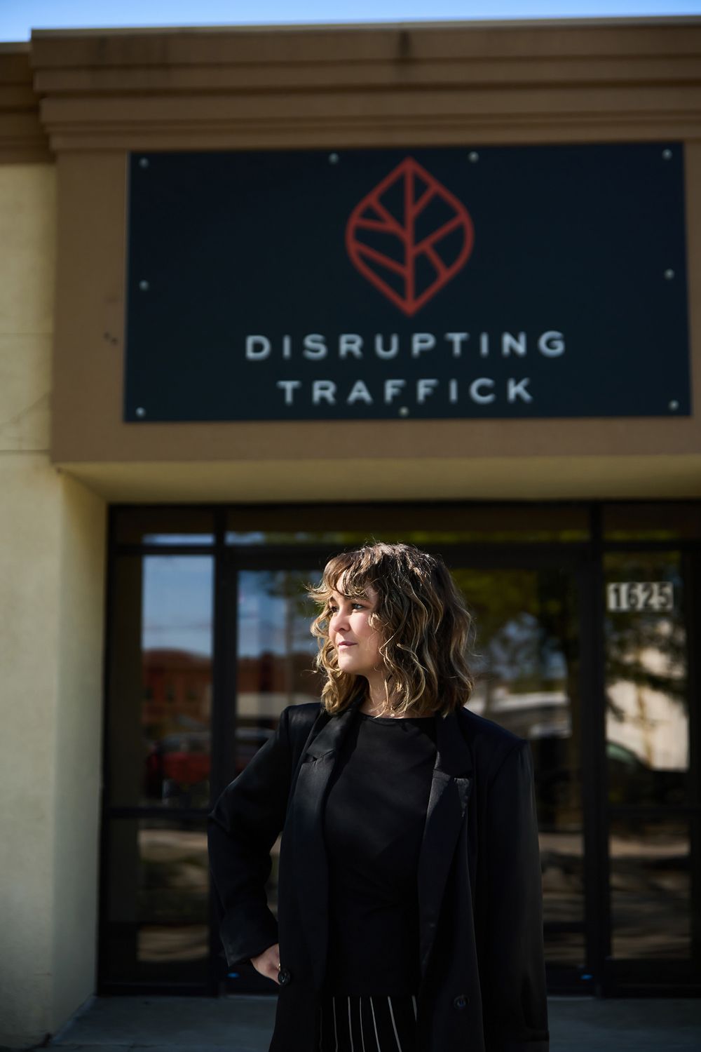 Woman in black outfit stands confidently outside Disrupting Traffick organization office building entrance.