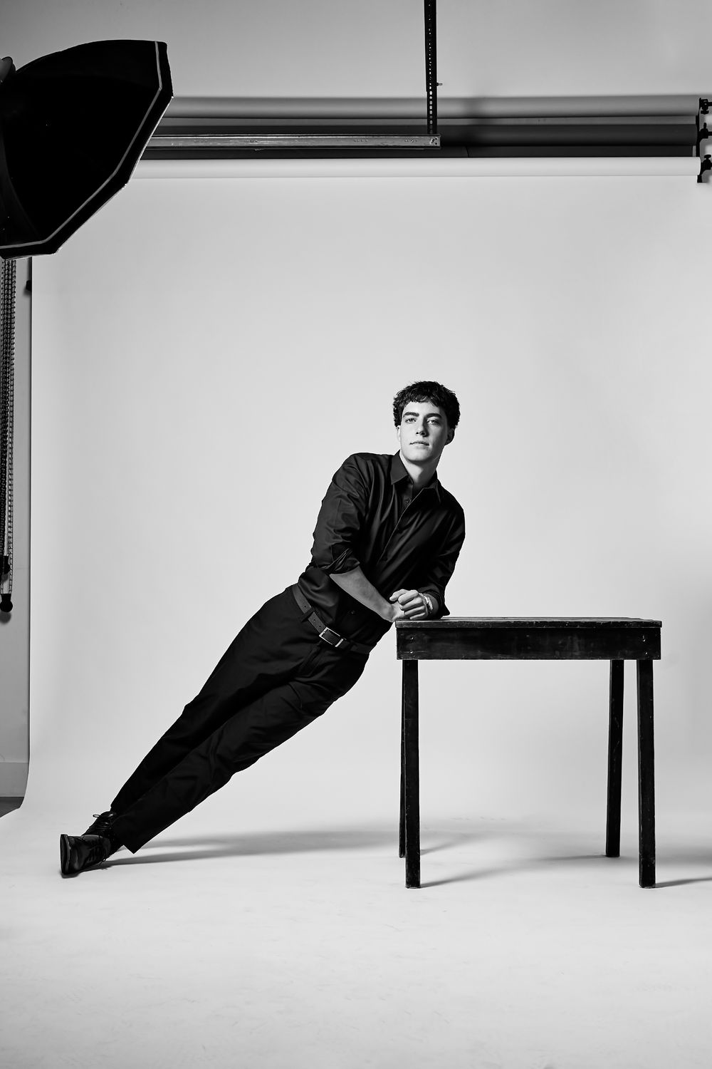 Artistic black and white photos of person in dark clothing posing with minimalist furniture.