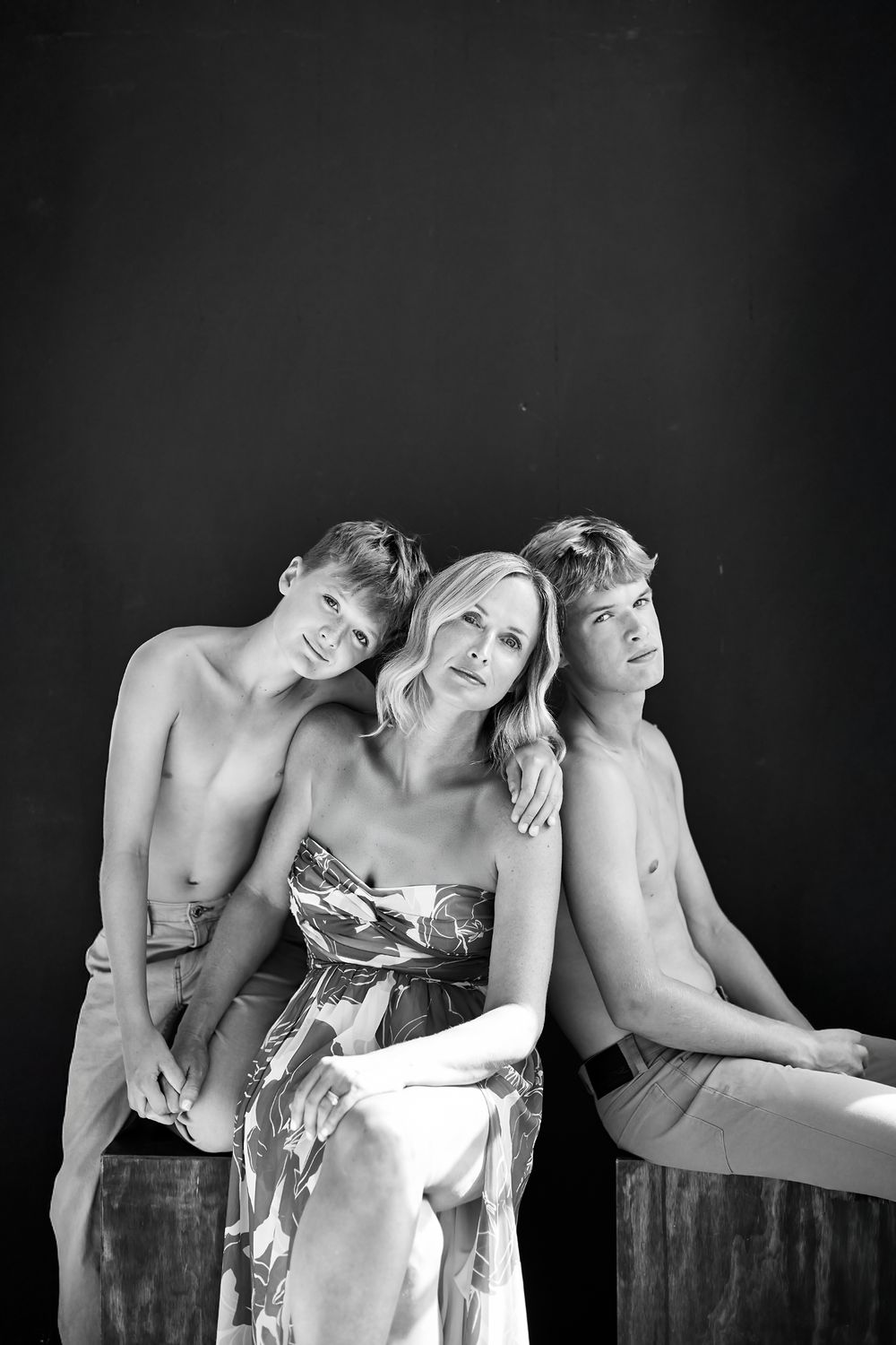 Black and white artistic portrait of three people in intimate poses against dark background.