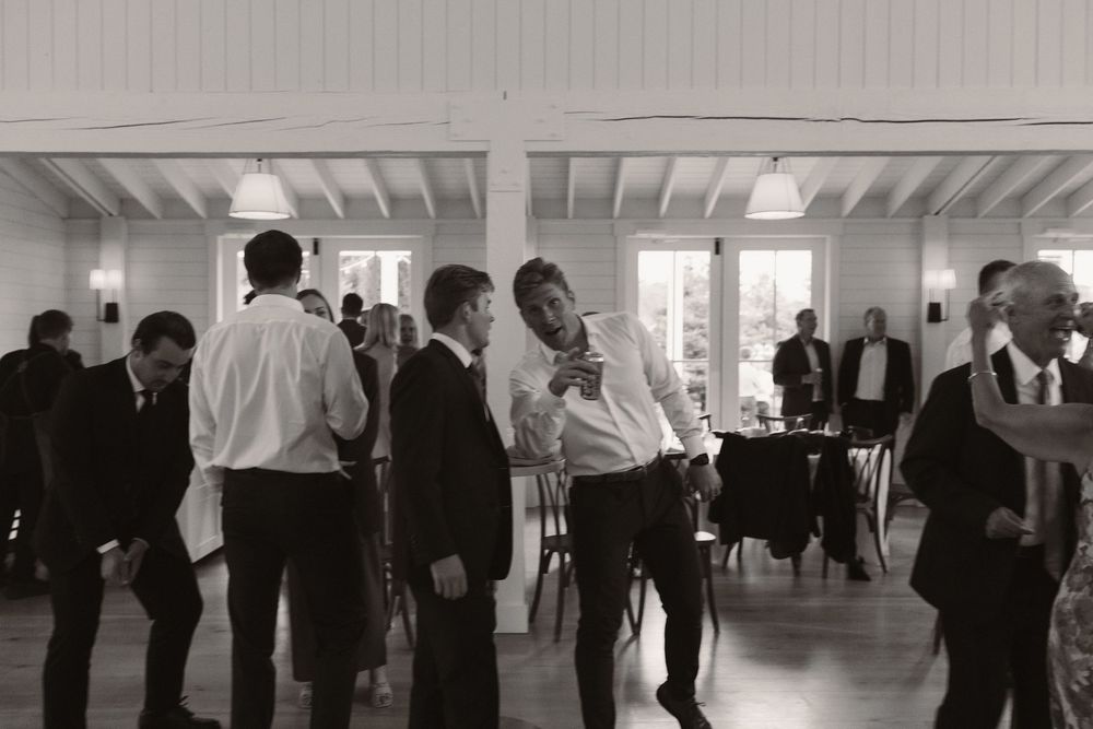 Wedding reception guests mingling in a spacious white-walled venue with natural lighting.