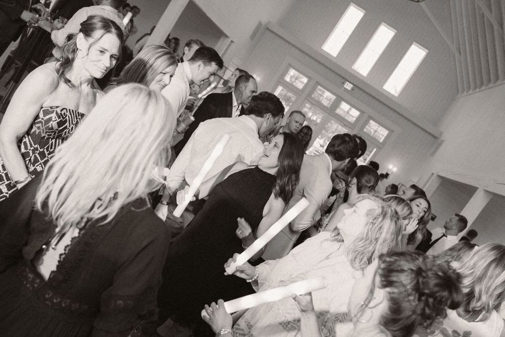 Black and white shot of wedding guests dancing and celebrating in a reception hall.